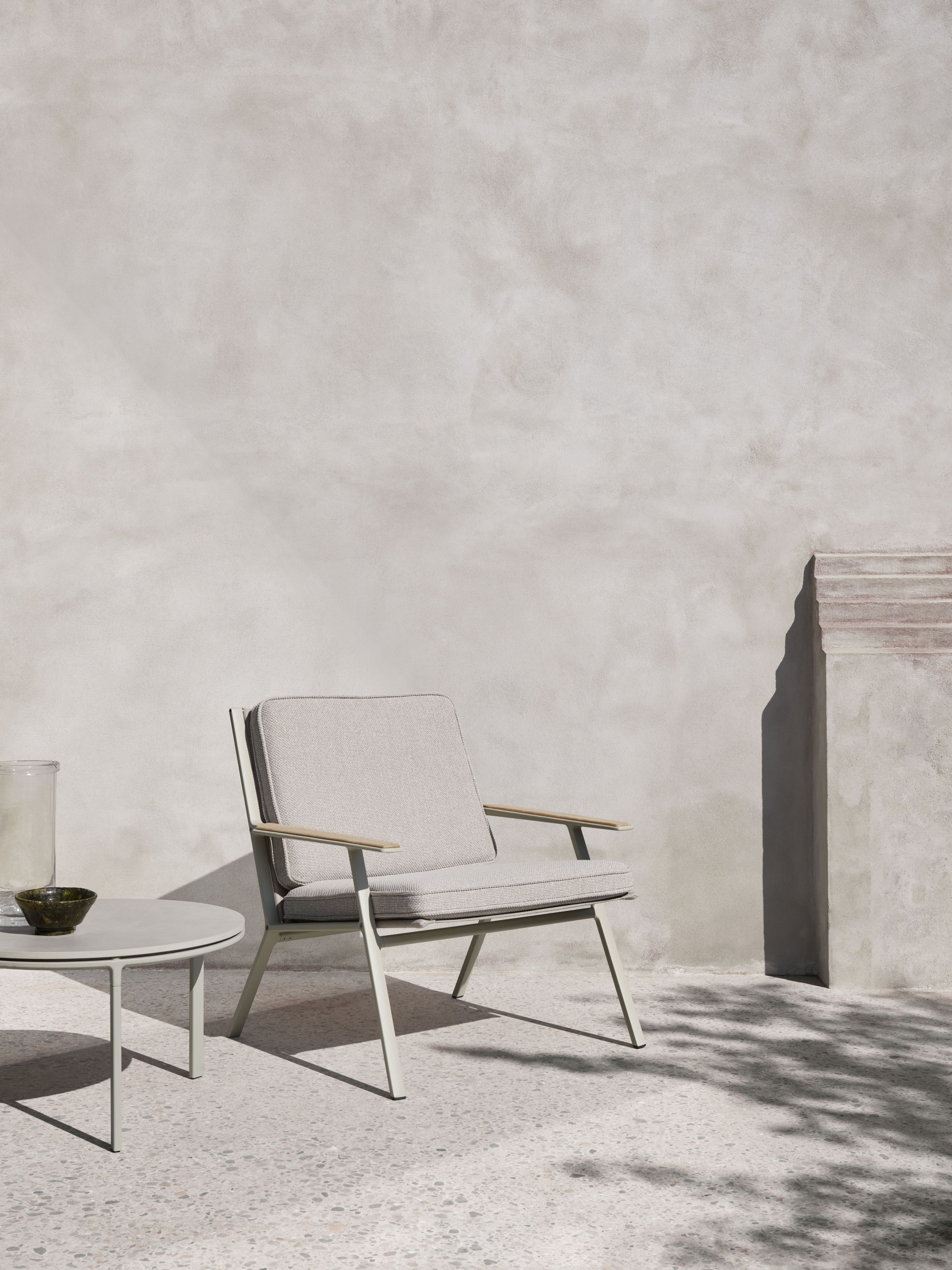 Heller Vipp Outdoor Lounge Stuhl mit Armlehnen und Tisch auf einer Terrasse.