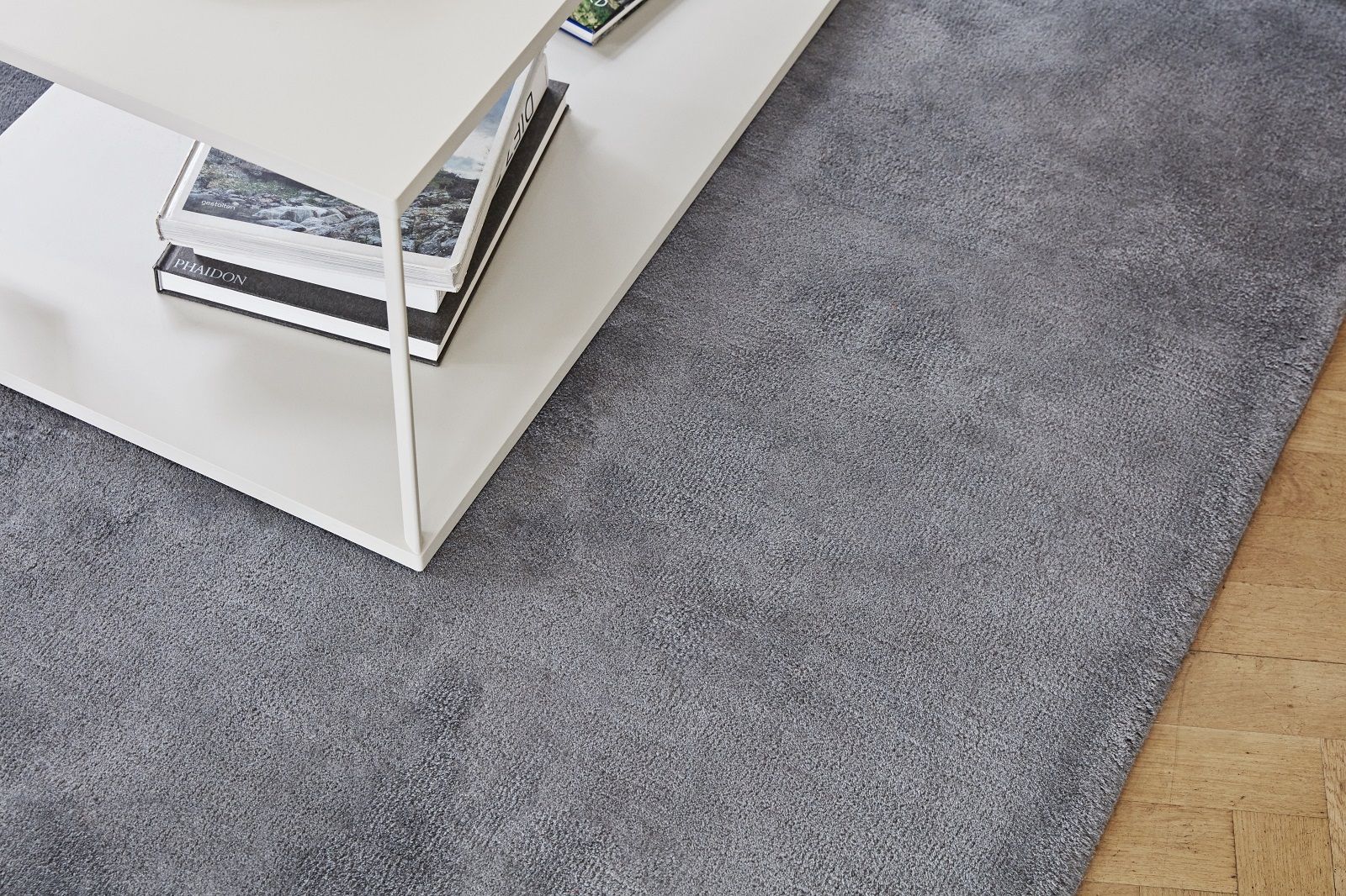 Nahaufnahme des grauen Hay Raw Rug No 2 Teppichs (300x200 cm) neben einem weißen Tisch.