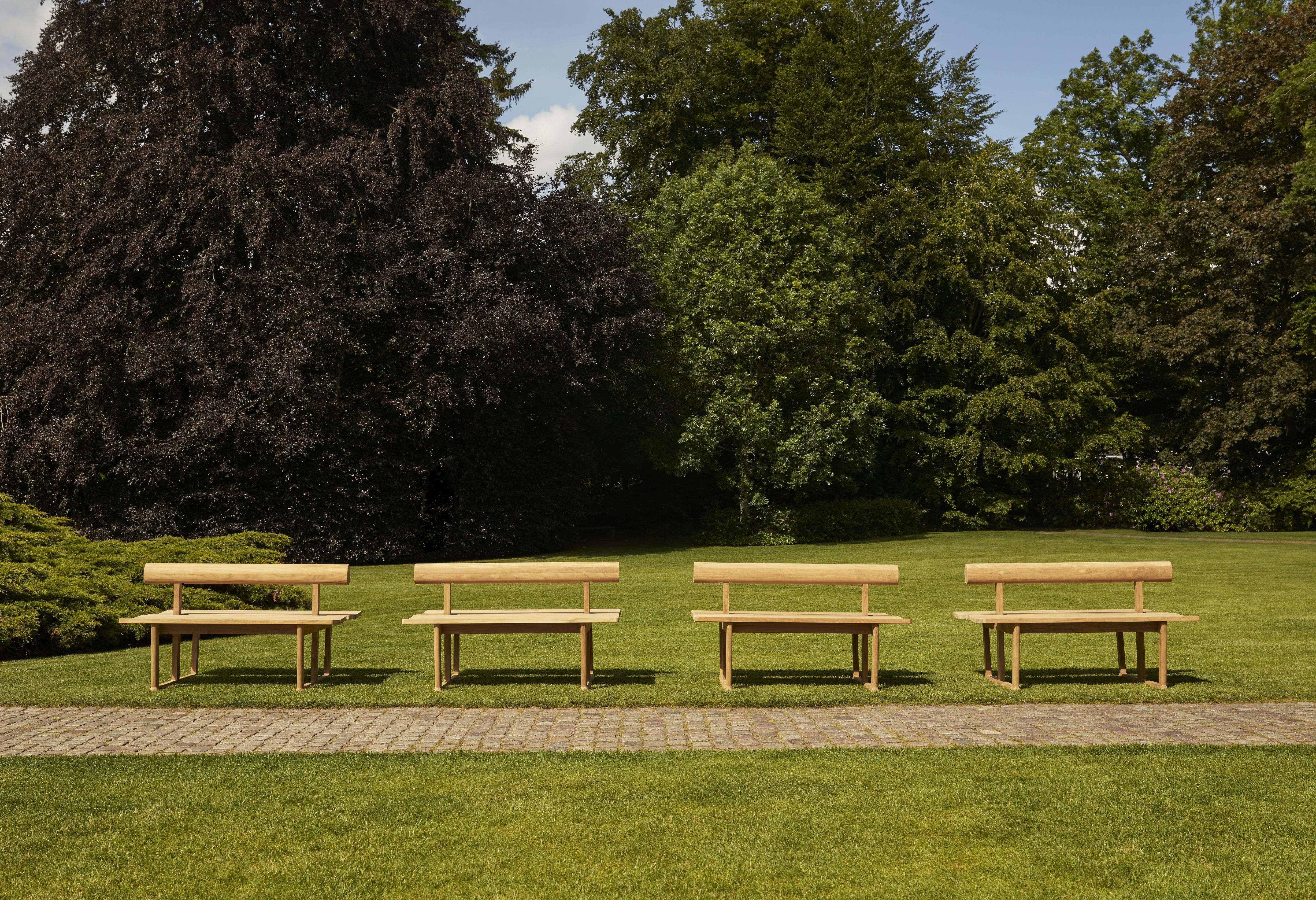 Vier Skagerak Teak Gartenbänke im Freien auf Rasen vor Bäumen. Outdoor Möbel.