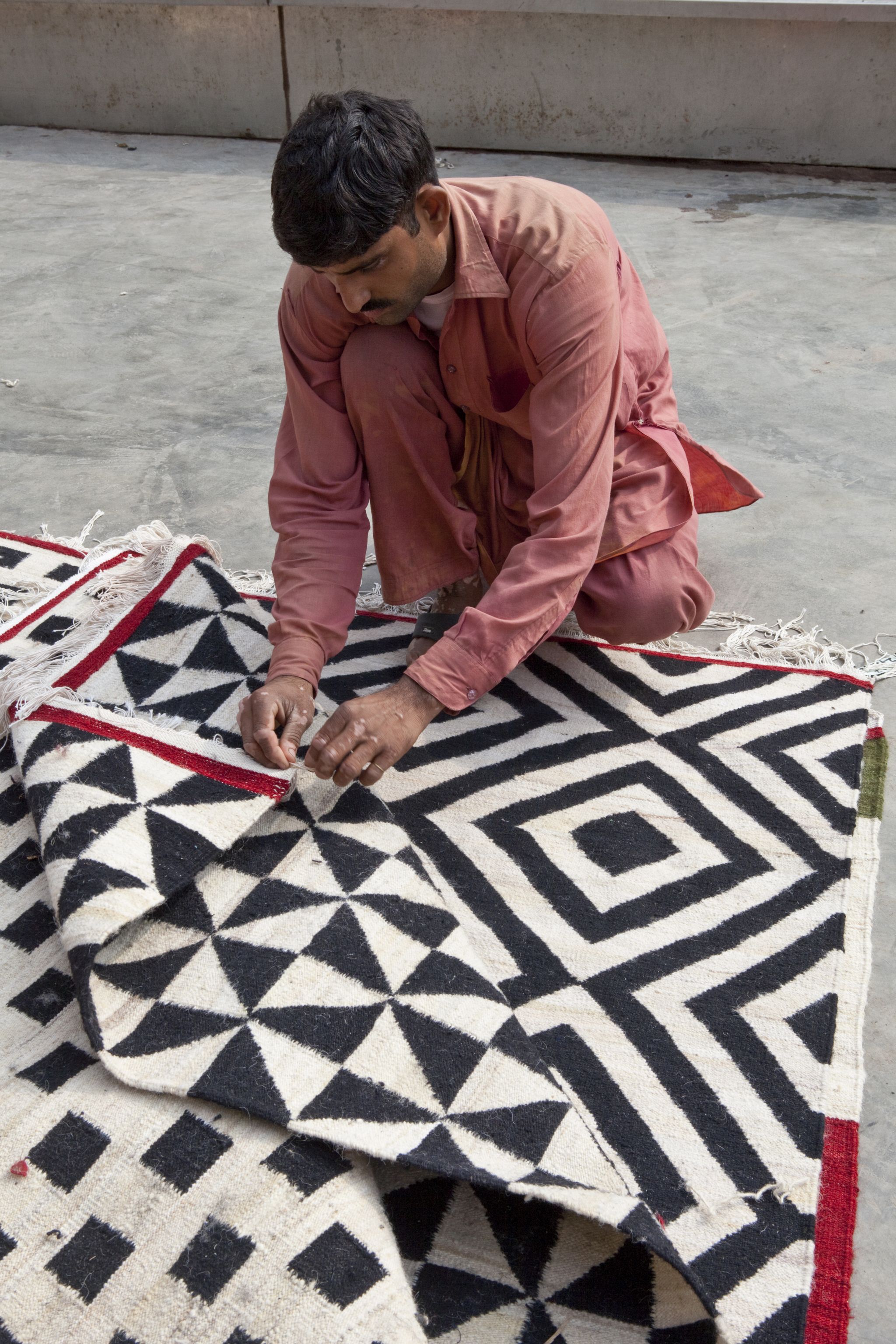 Mann fertigt Nanimarquina Mélange Pattern Teppich, 80x240 cm, mit geometrischem Muster und Fransen.