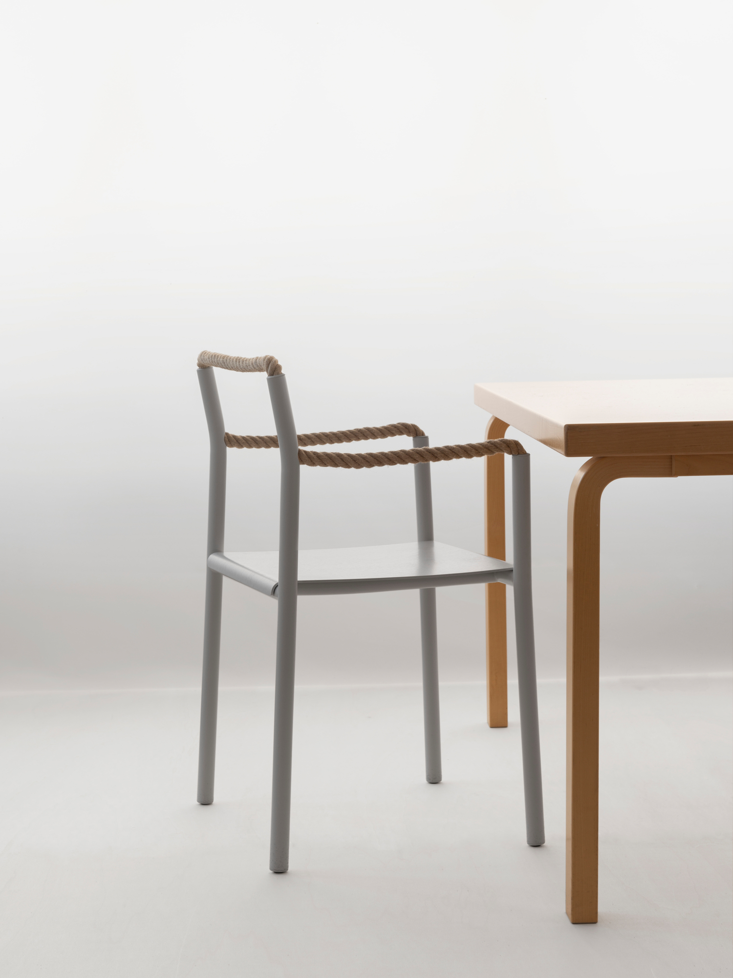 Artek Rope Chair Stuhl mit grauem Gestell und Seil-Detail neben einem Holztisch.