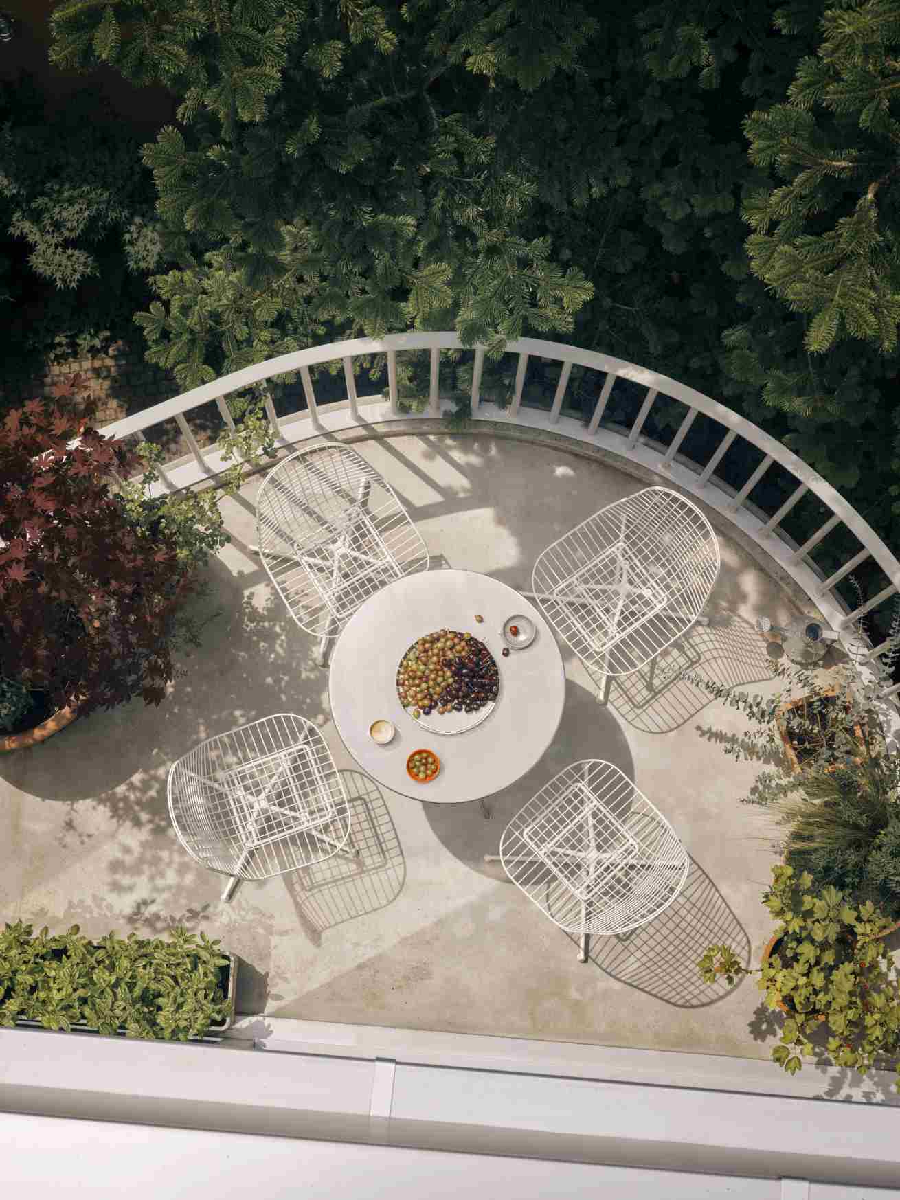 Vogelperspektive: Weißer Vitra DKL Wire Chair Stuhl um runden Tisch auf sonniger Terrasse.