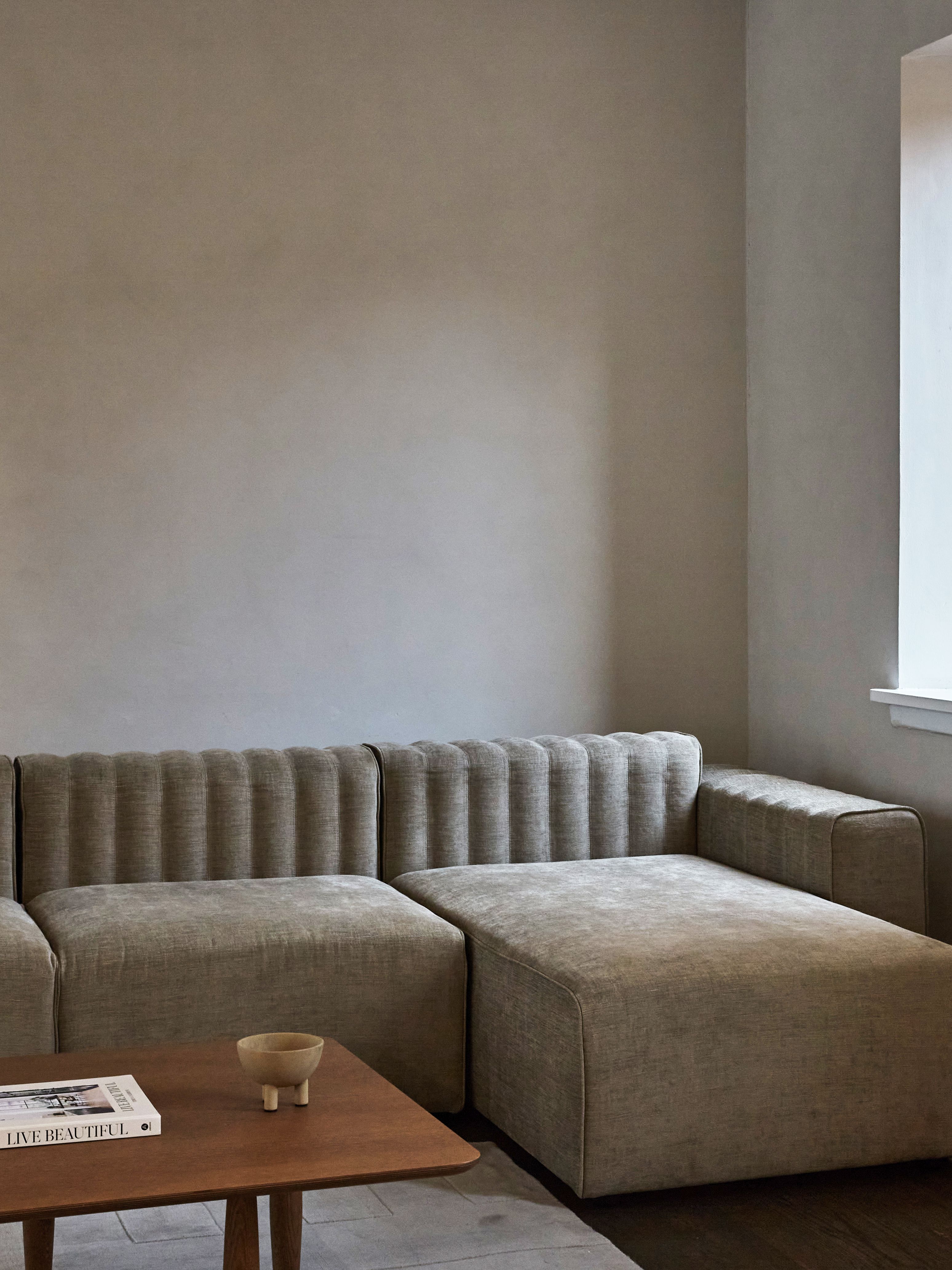 Oku Couchtisch Eiche hell geräuchert von Norr11 neben einem beigen Sofa und Dekoration.