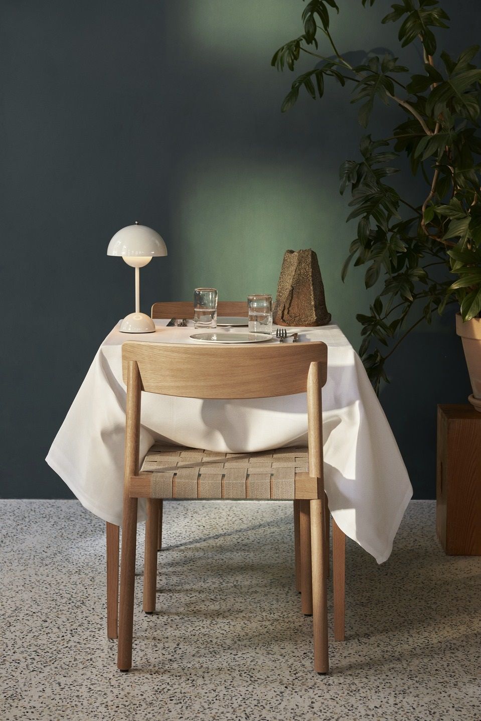 AndTradition Betty TK1 Stuhl aus Holz mit gewebter Sitzfläche vor gedecktem Tisch.