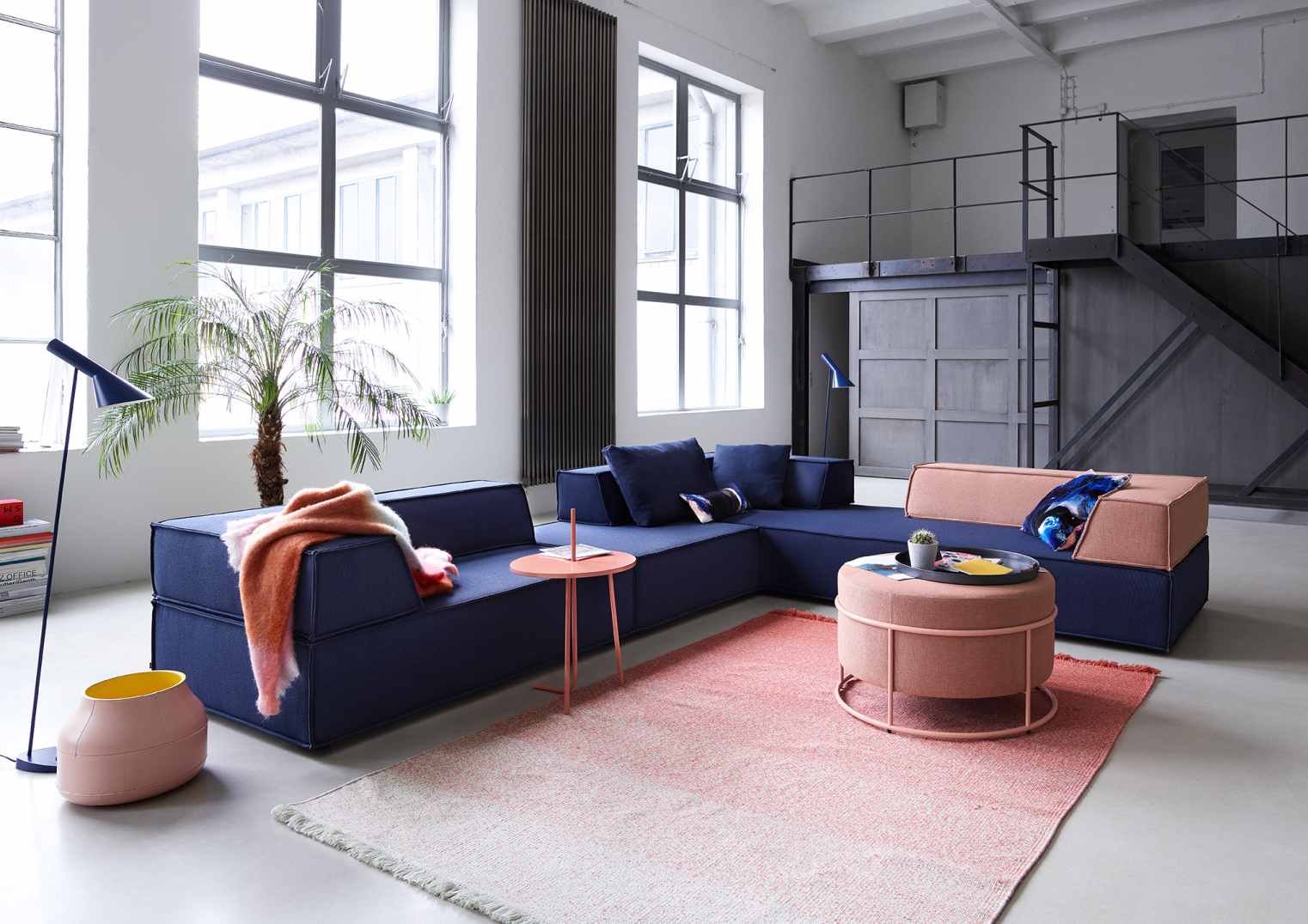 Modernes Wohnzimmer mit blauer Modulcouch, rosa Teppich und Beistelltisch, helle Loft-Atmosphäre.