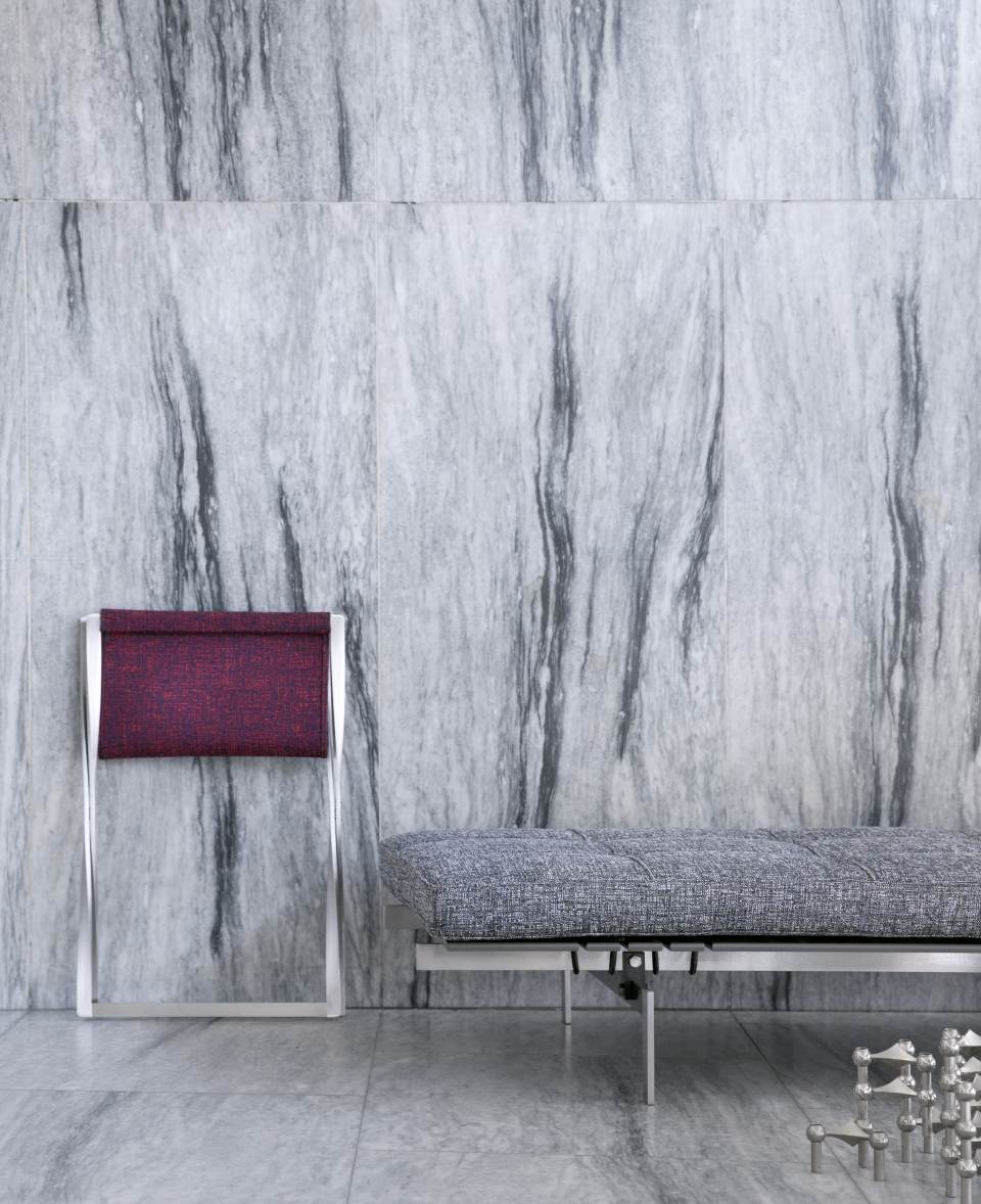 PK 80 Liege von Fritz Hansen mit grauem Bezug und passendem Hocker vor Marmorwand.