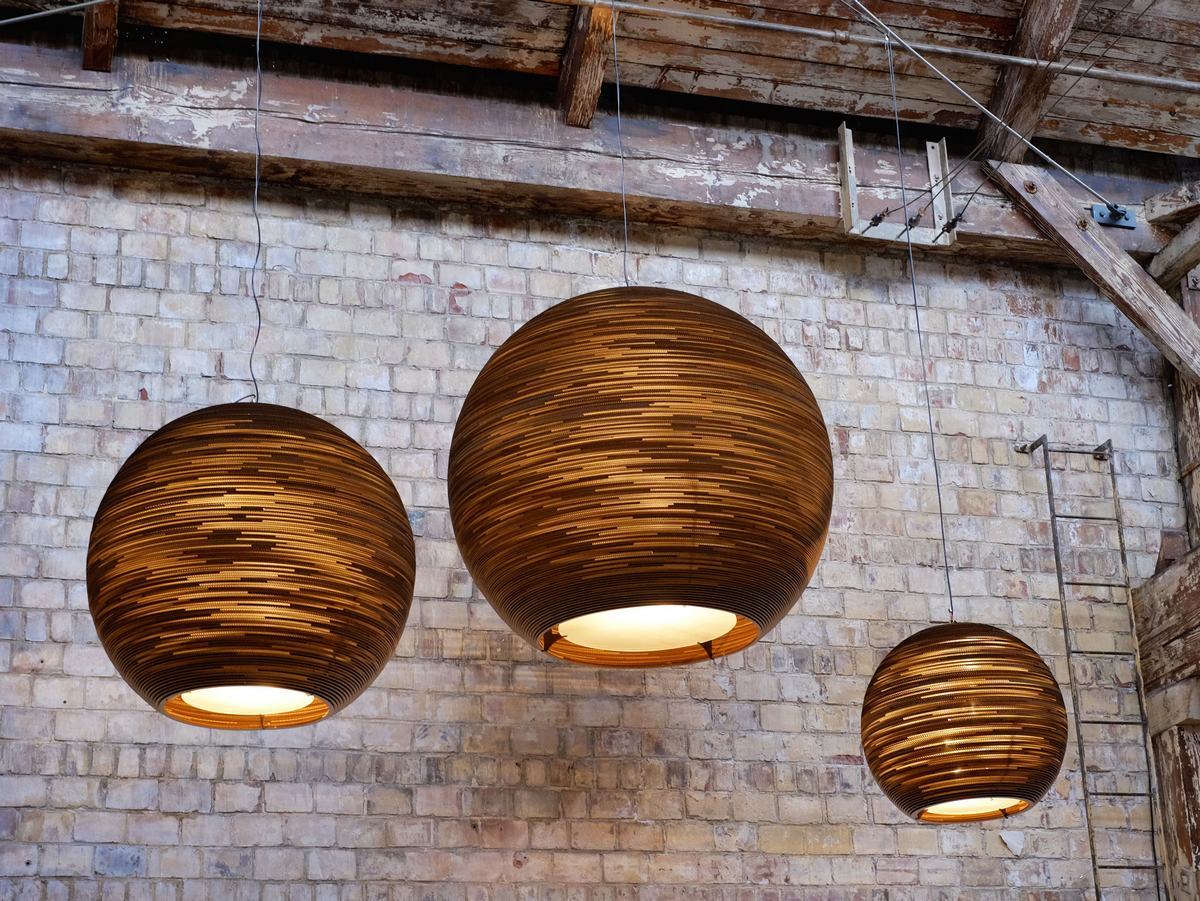 Drei Sun32 Scraplights Hängeleuchten von Graypants, gefertigt aus recyceltem Karton, vor einer Backsteinwand.
