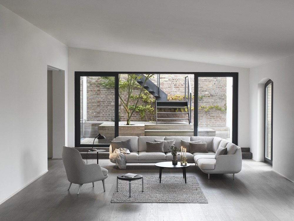 Heller Wohnraum mit grauem PK33 Hocker von Fritz Hansen, Sessel und großem Ecksofa.