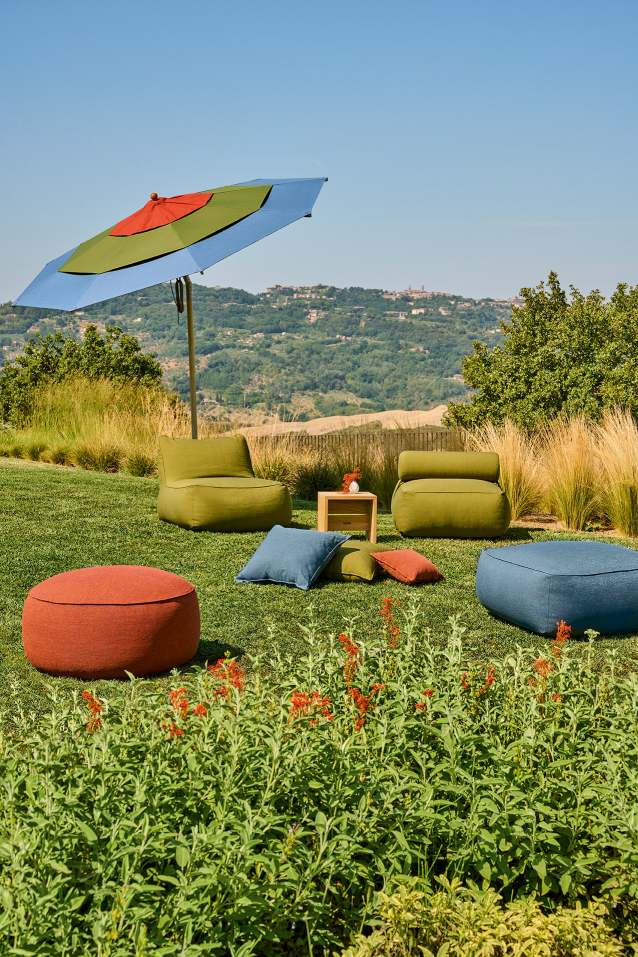 Weishäupl Klassiker Sonnenschirm über Outdoor-Lounge-Bereich mit Poufs und Sesseln im Garten, ideal für entspannte Sommertage.