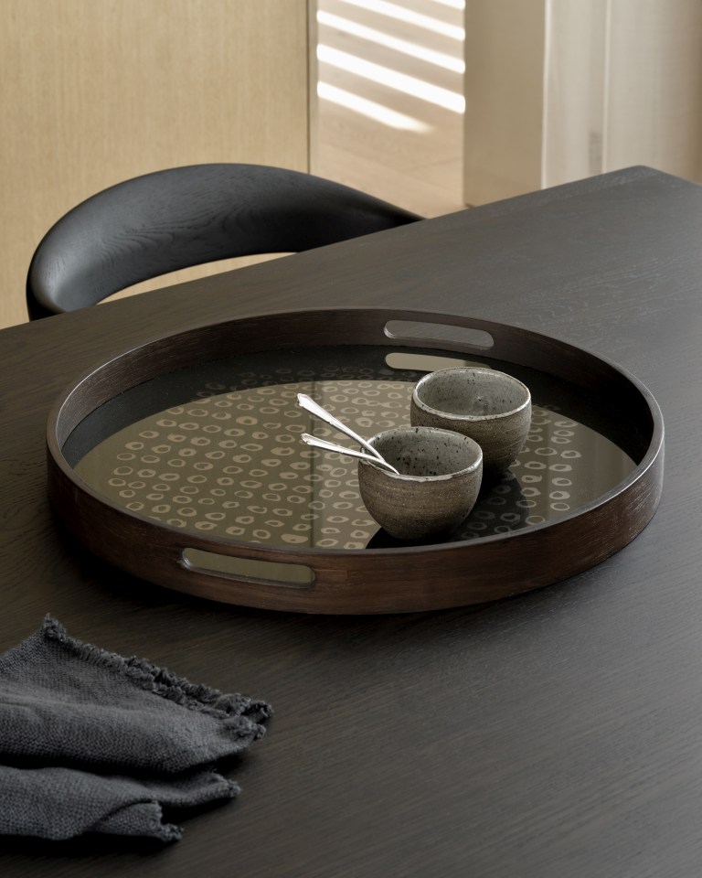 Rundes Holztablett "Second Nature Tray" von Ethnicraft mit Muster und zwei Schalen auf dunklem Tisch.