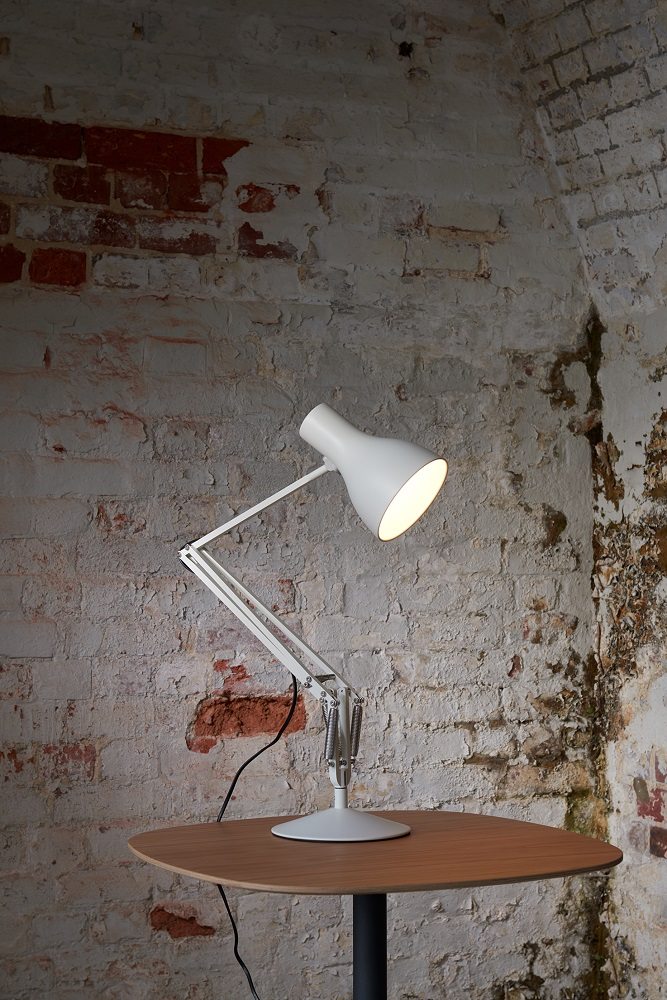 Anglepoise Type 75 Schreibtischleuchte in Alpinweiß auf Holztisch vor rustikaler Backsteinwand.