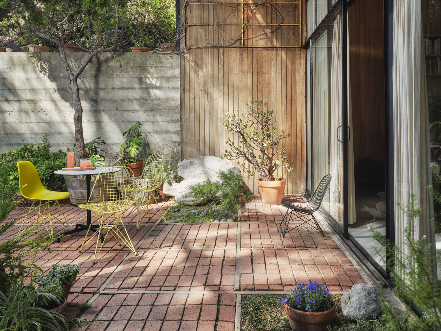 Gelbe und schwarze DKR Wire Chairs von Vitra mit Sitzkissen im Garten auf Backsteinboden.