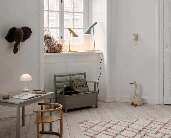 Kinderzimmer mit Schreibtisch, Tischleuchte, Banktruhe und dekorativen Elementen wie Elefant, Gans und Lampen.