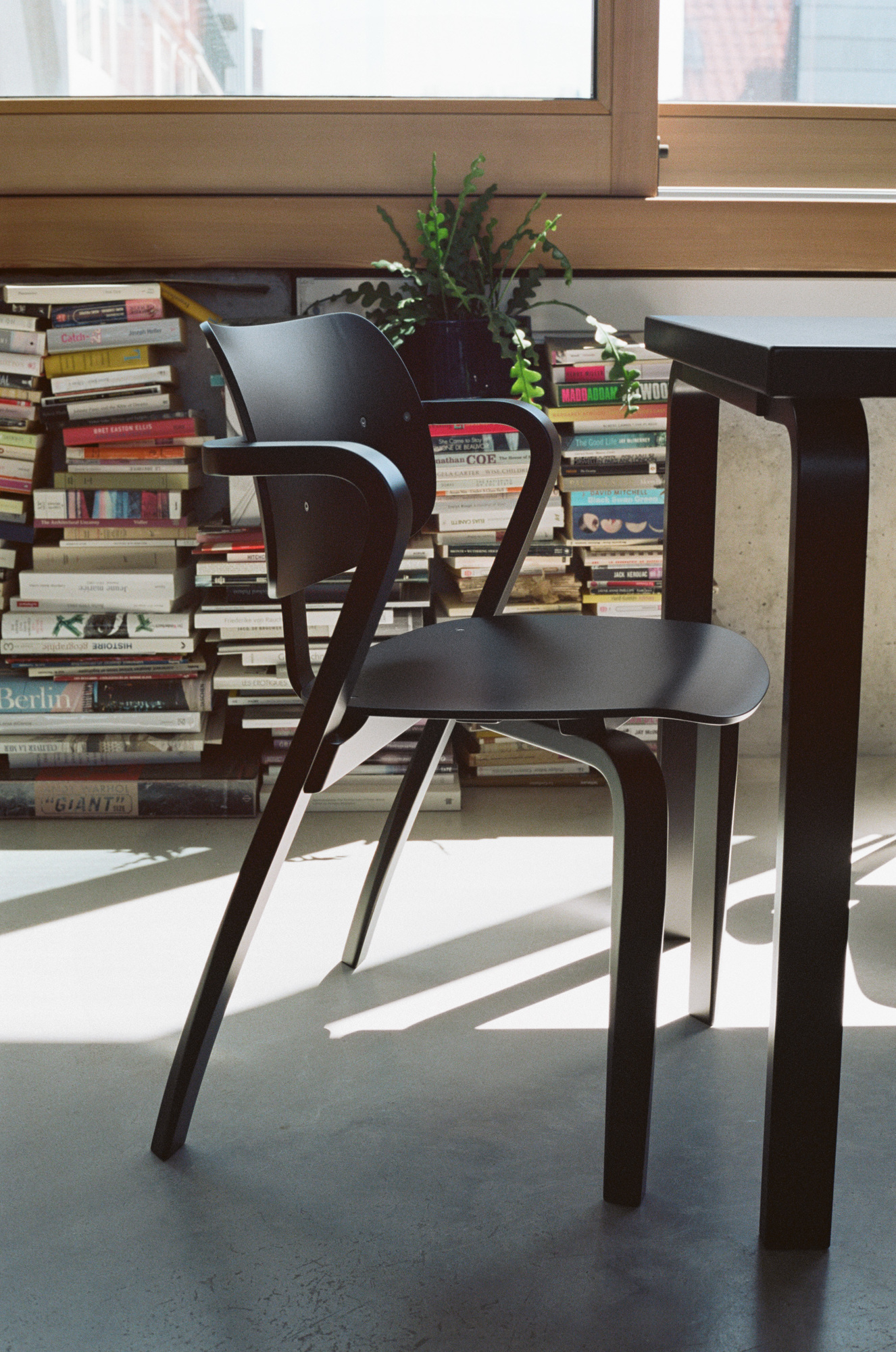 Schwarzer Aslak Chair Stuhl von Artek vor Bücherwand und Fenster, modernes Möbeldesign für Wohnzimmer und Büro.