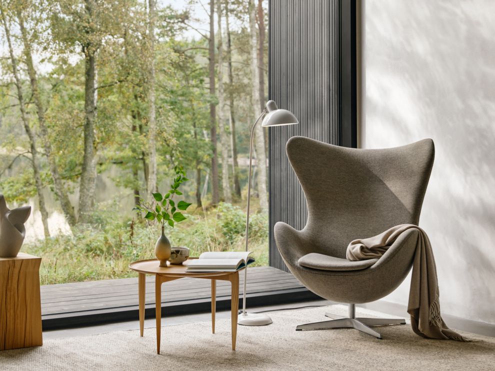 Fritz Hansen Tray Beistelltisch Ø60cm aus Holz neben Sessel und Fenster mit Blick in die Natur.