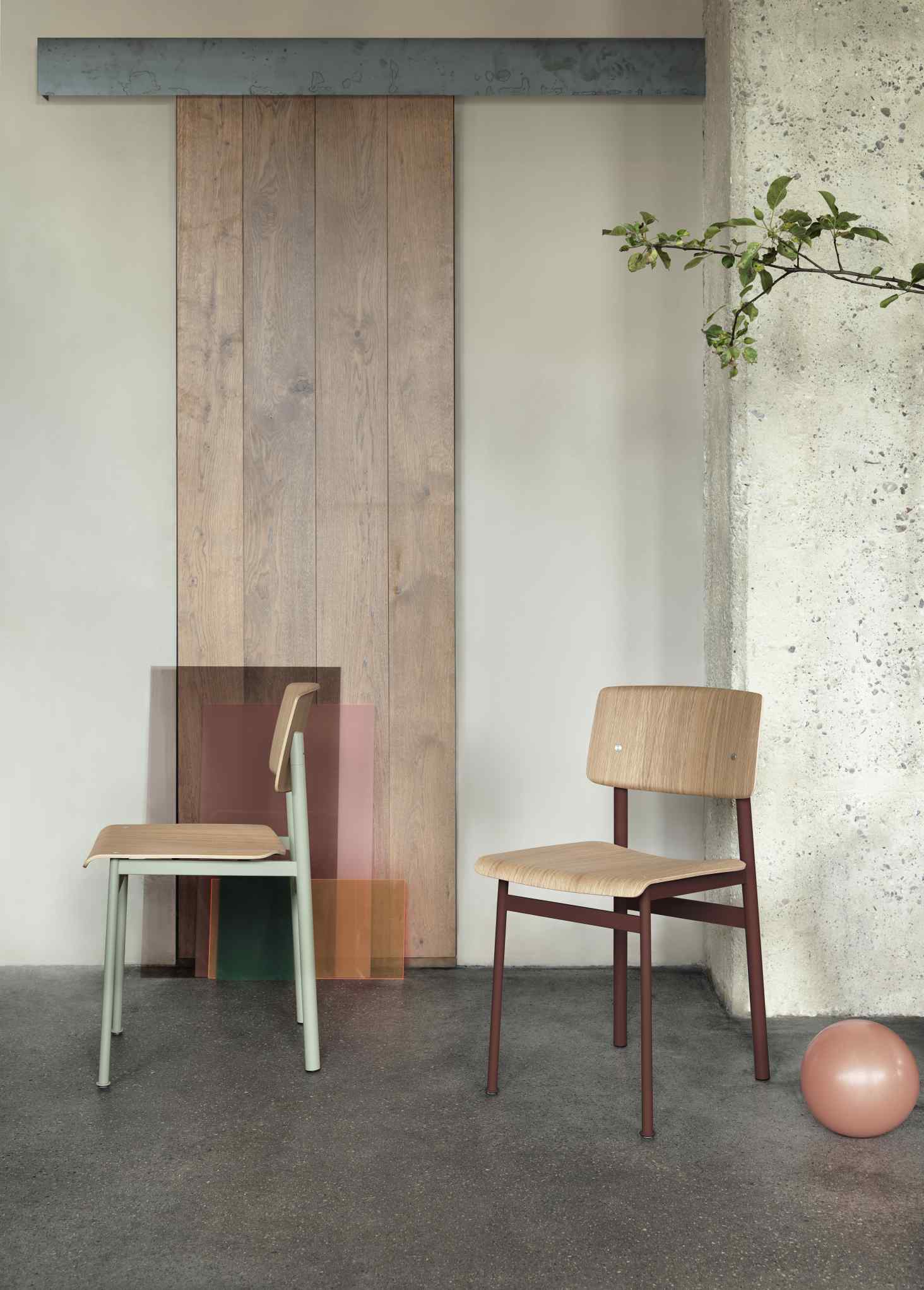 Zwei Muuto Loft Chair Stühle in Mintgrün und Braun vor Holztür und Betonwand.