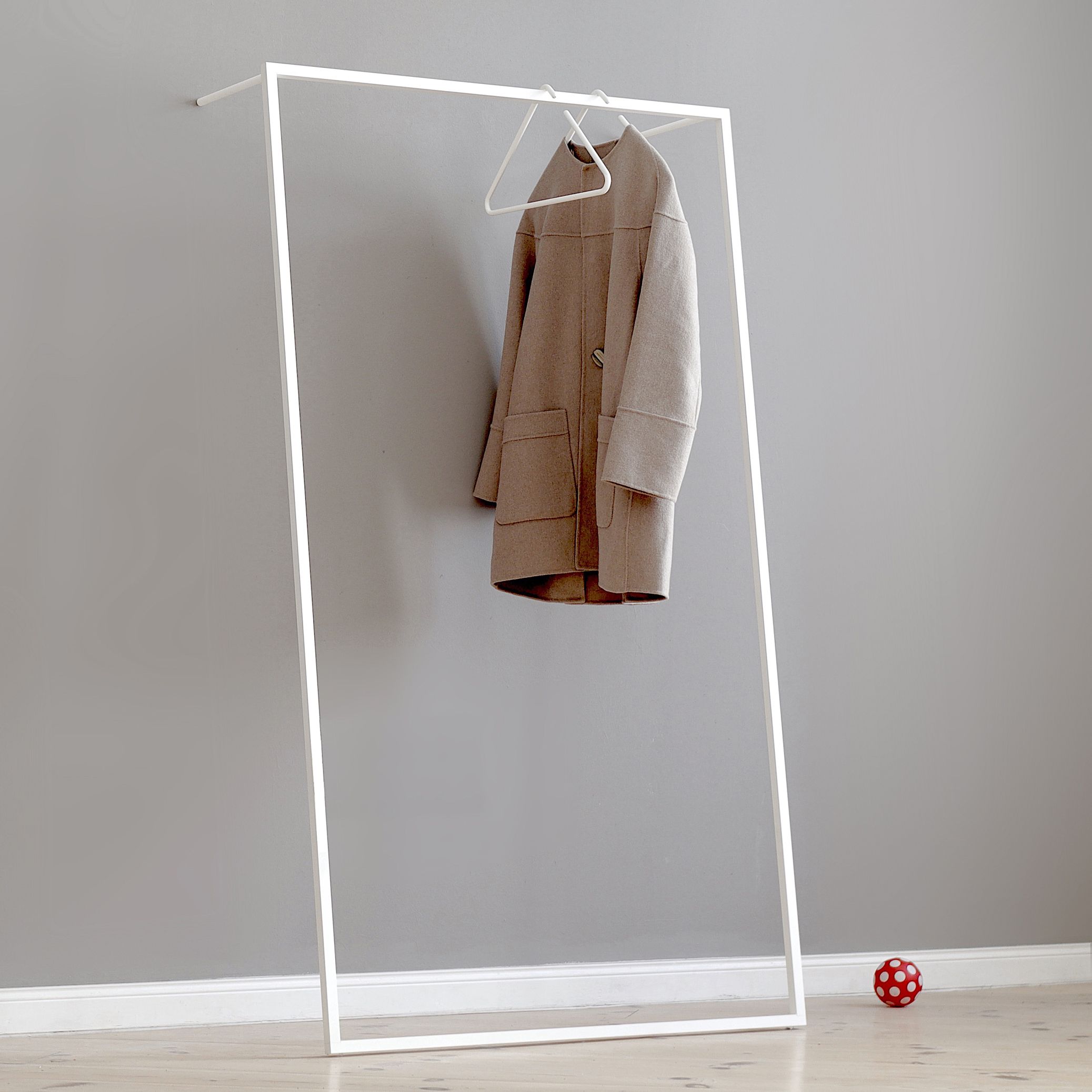 Weiße Leano Anlehngarderobe von Roomsafari mit Mantel an Kleiderbügel vor grauer Wand. Moderne Garderobenlösung.