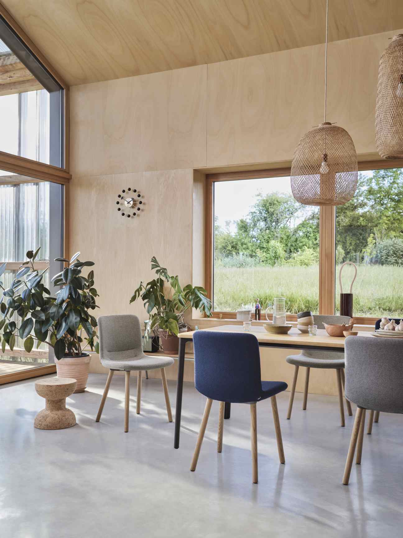 Esszimmer mit Esstisch, Stühlen in Grau und Blau, Hängelampen und Blick ins Grüne.