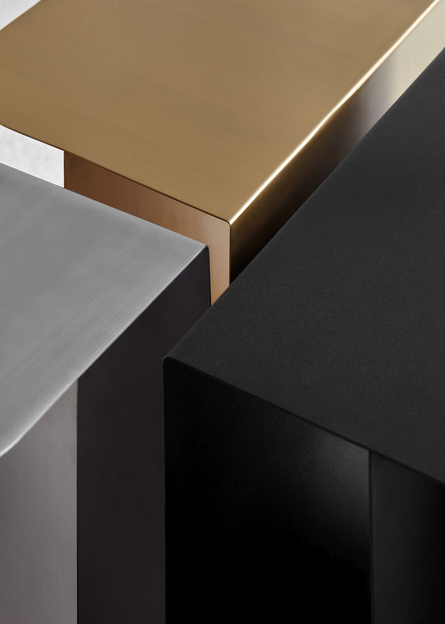 Detailaufnahme von drei Mass Beistelltischen aus Stahl in Schwarz, Gold und Silber.