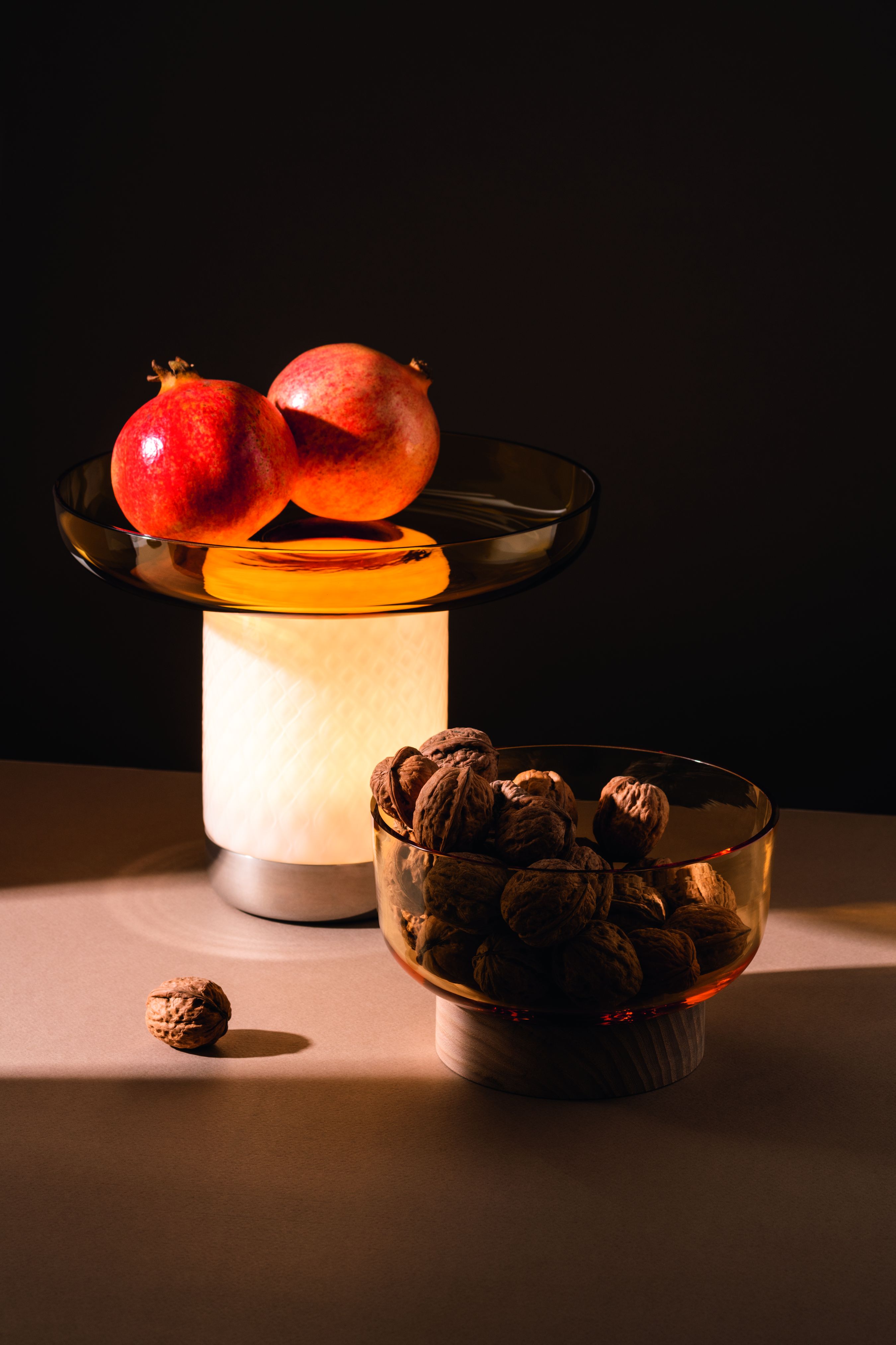 Bontà Akkuleuchte von Artemide mit Granatäpfeln und Walnüssen in Glasschalen für stimmungsvolle Beleuchtung.
