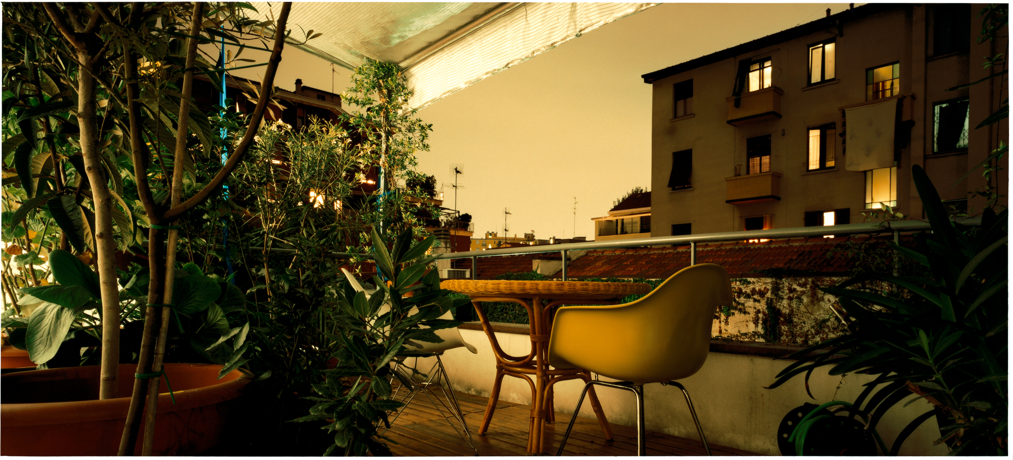 Gelber Eames Plastic Arm Chair DAR Stuhl von Vitra auf einem begrünten Balkon bei Nacht.