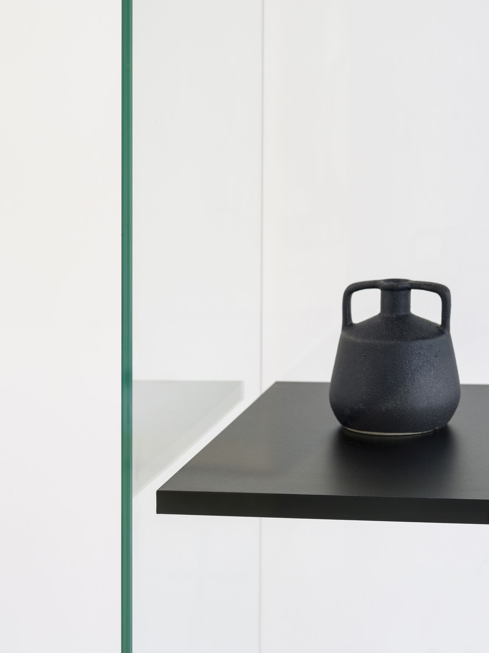 Stolp Low Vitrine Functionals: Detailaufnahme einer schwarzen Keramikvase auf einem schwarzen Regalbrett vor weißer Wand.