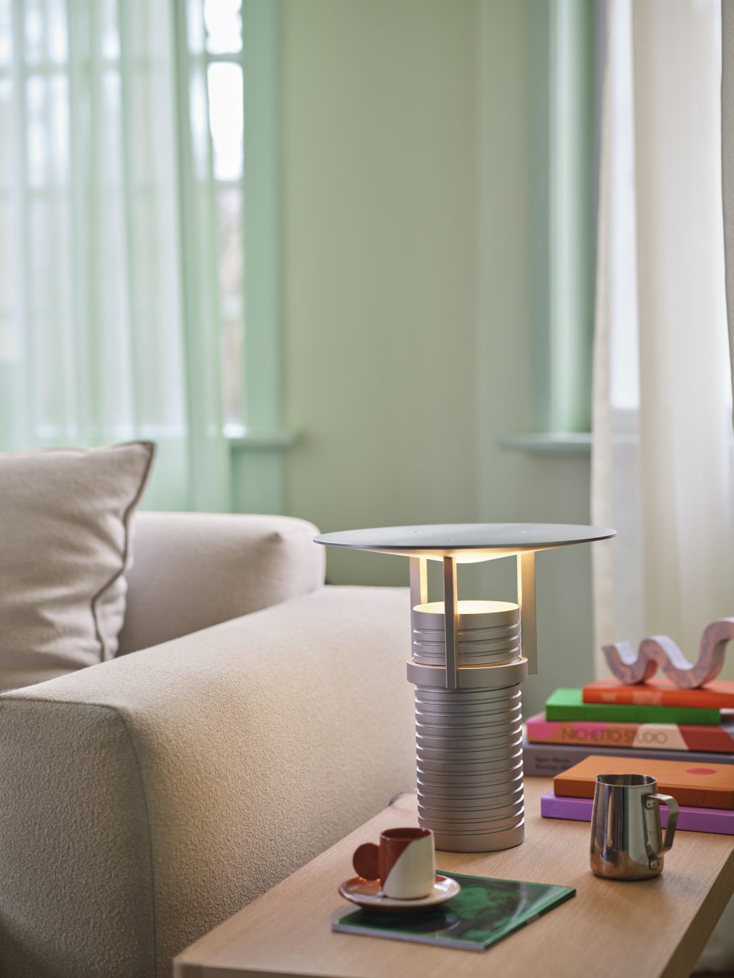 Beiges Muuto Sofa (2-Sitzer) mit Kissen im Wohnzimmer, neben einer modernen Tischleuchte.