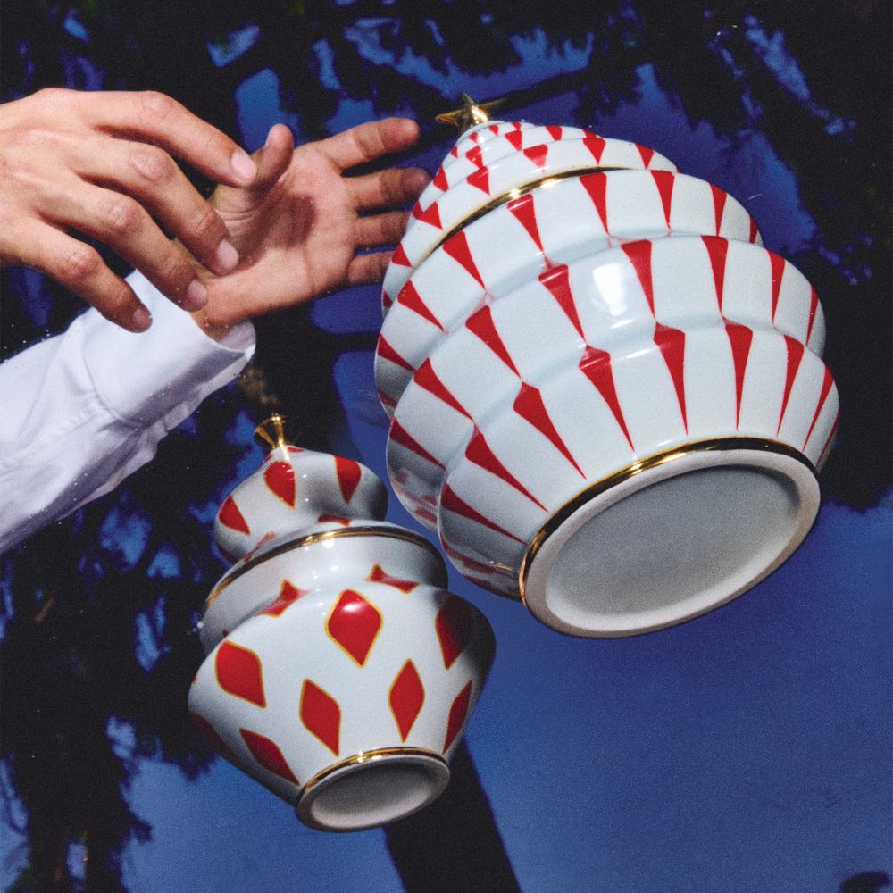 Alessi Delight Süßigkeitenbehälter NZ03 mit rotem Muster und goldenen Akzenten, schwebend vor blauem Hintergrund.