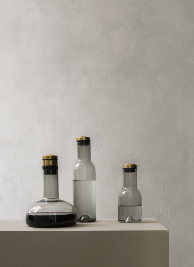 Wine Breather Collection: Drei graue Glaskaraffen mit goldenen Deckeln, eine mit Rotwein gefüllt, auf einem Podest.