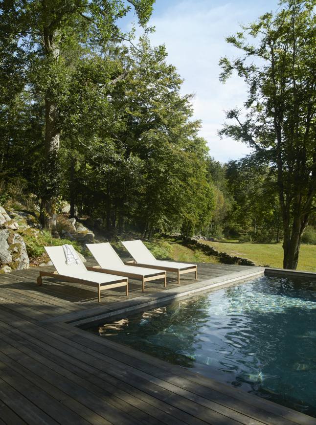 Drei Pelagus Sonnenliegen von Skagerak by Fritz Hansen stehen auf einer Holzterrasse neben einem Pool im Garten.