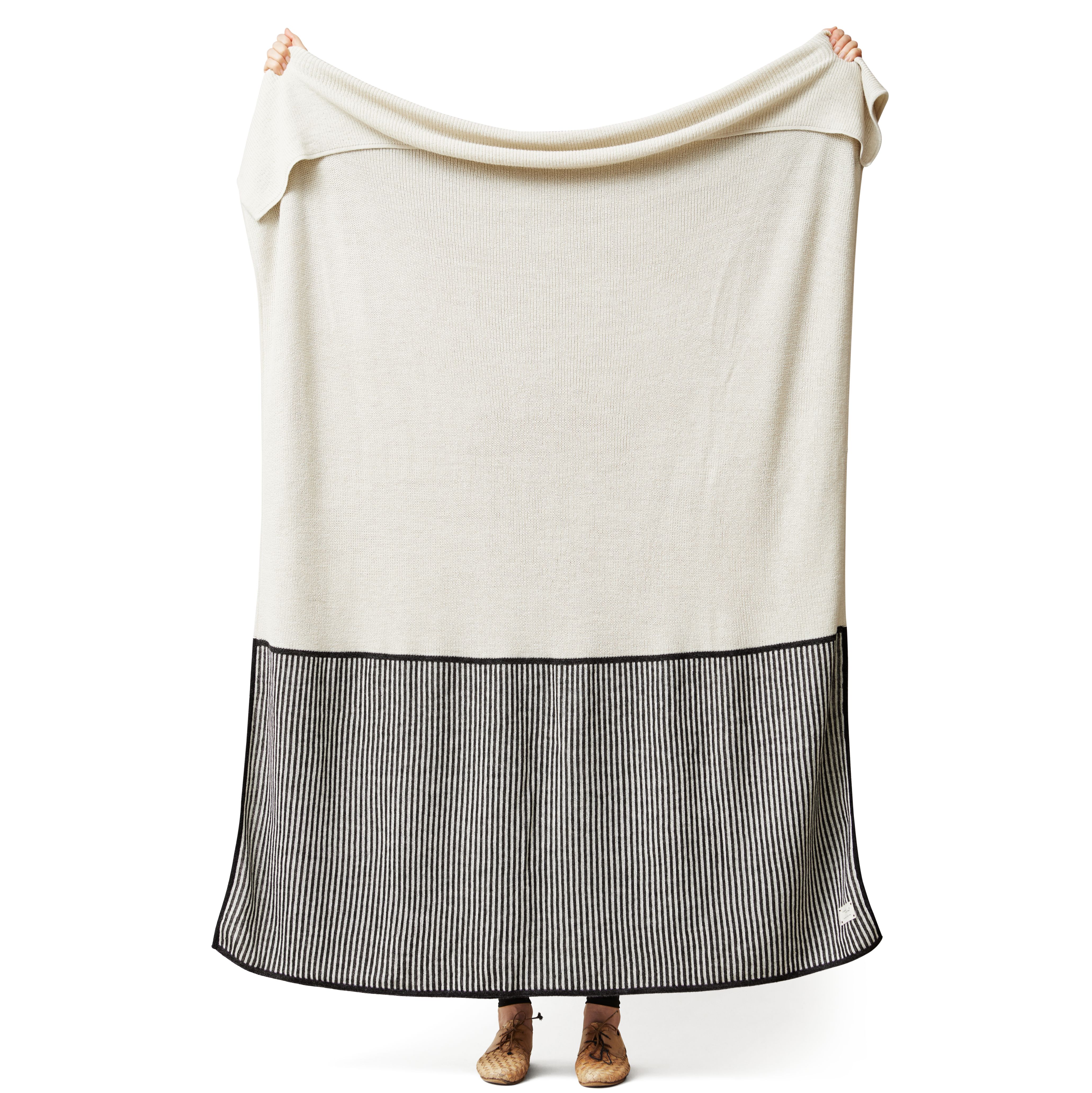 Aymara Decke in Creme mit schwarzen Streifen, gehalten von zwei Händen. Kuscheldecke für Zuhause.