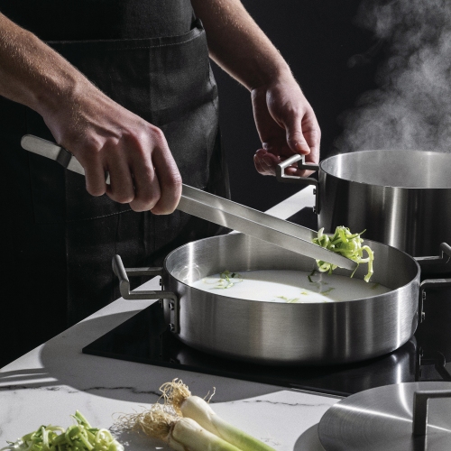 DC07S4 Convivio Alessi Küchenset: Koch bereitet mit Zange und Topf Gemüse in der Küche zu.