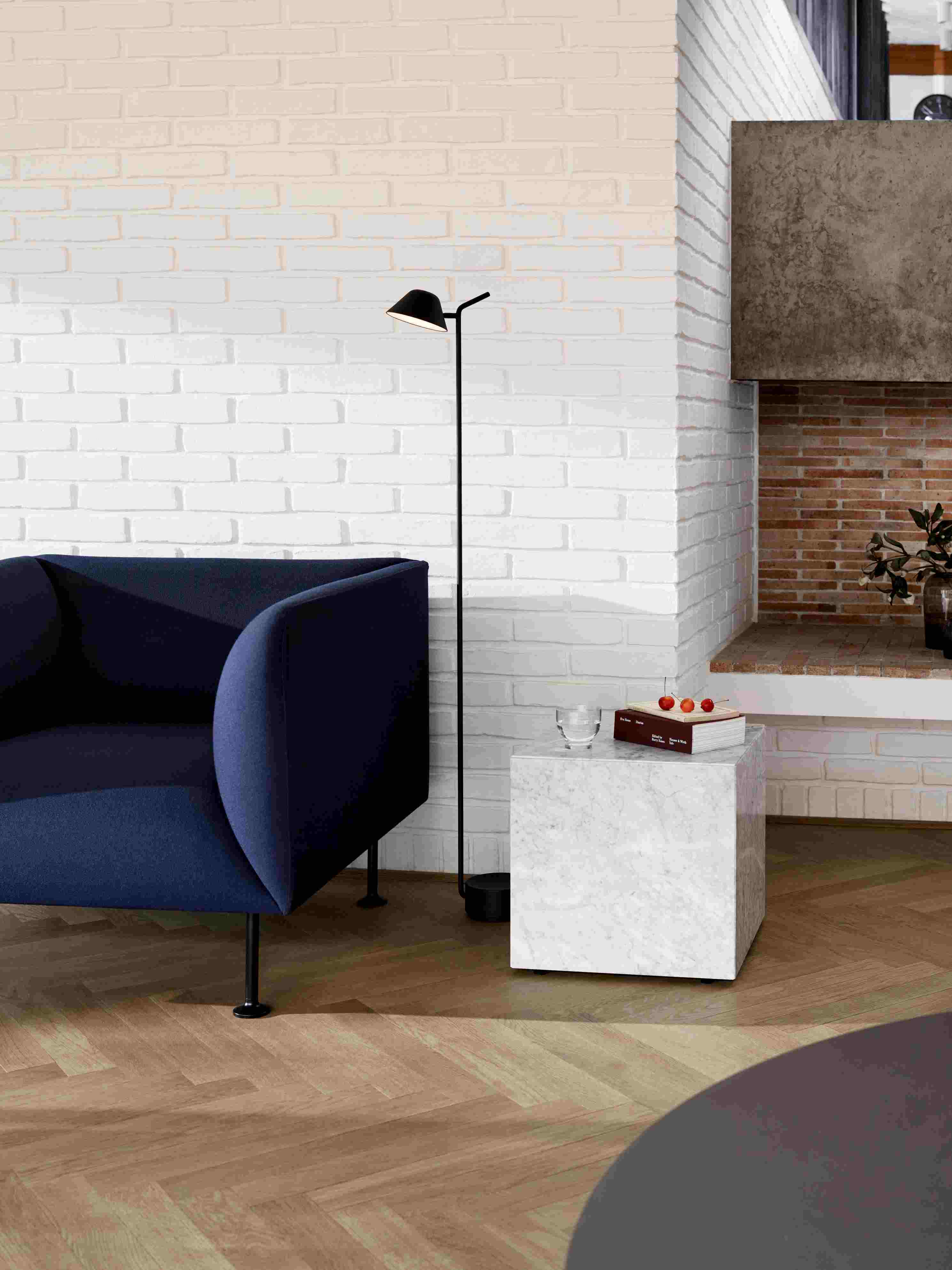 Audo Copenhagen Plinth Tisch aus Marmor neben blauem Sessel und Stehlampe im Wohnzimmer.