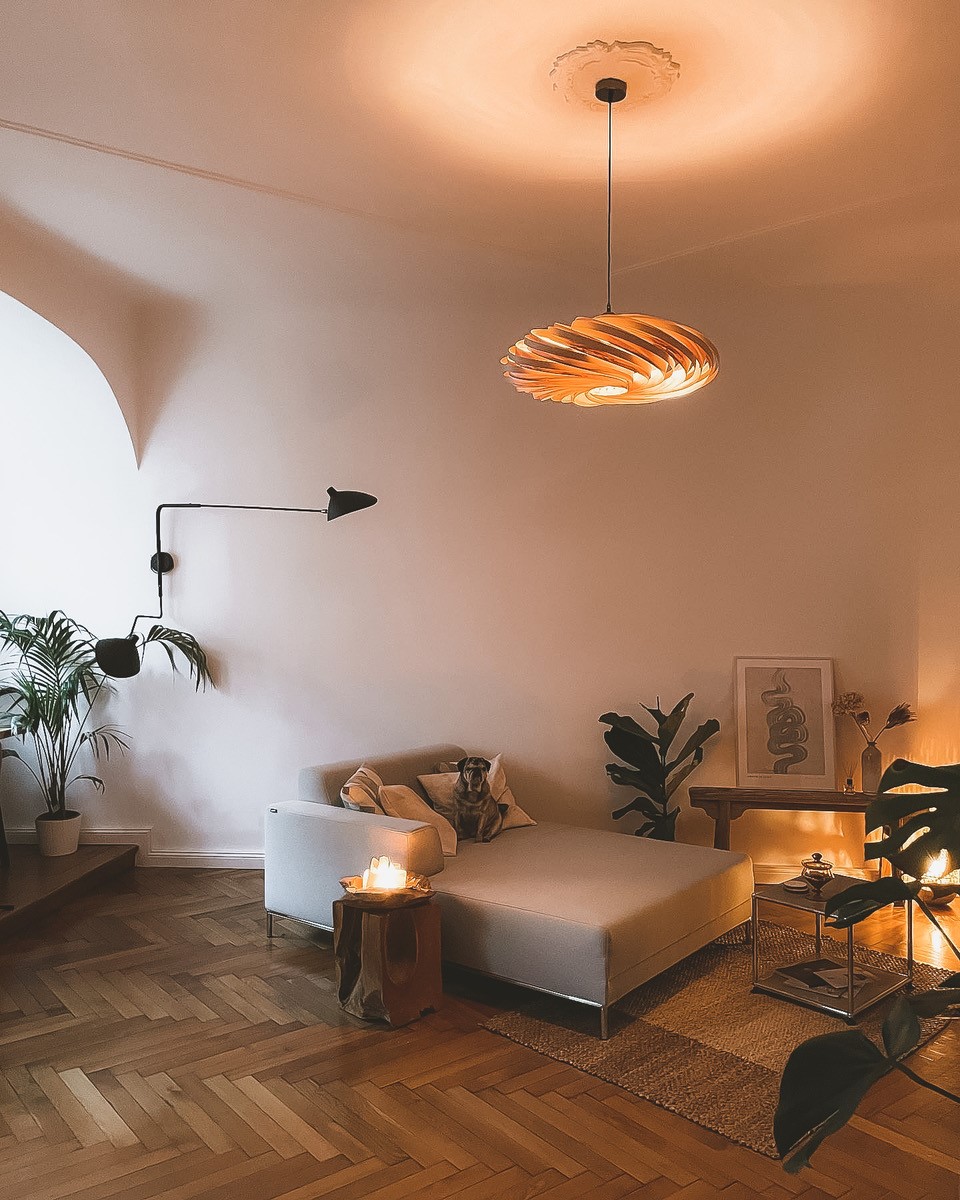 Wohnzimmer mit moderner Holzlampe, beigem Sofa, Holzboden und Hund für gemütliche Atmosphäre.