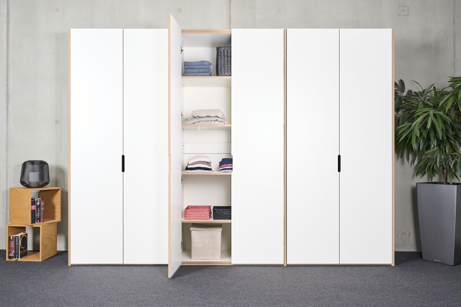 Tojo Schrank Anbaumodul mit weißen Türen, Regalböden und Textilien im geöffneten Zustand.