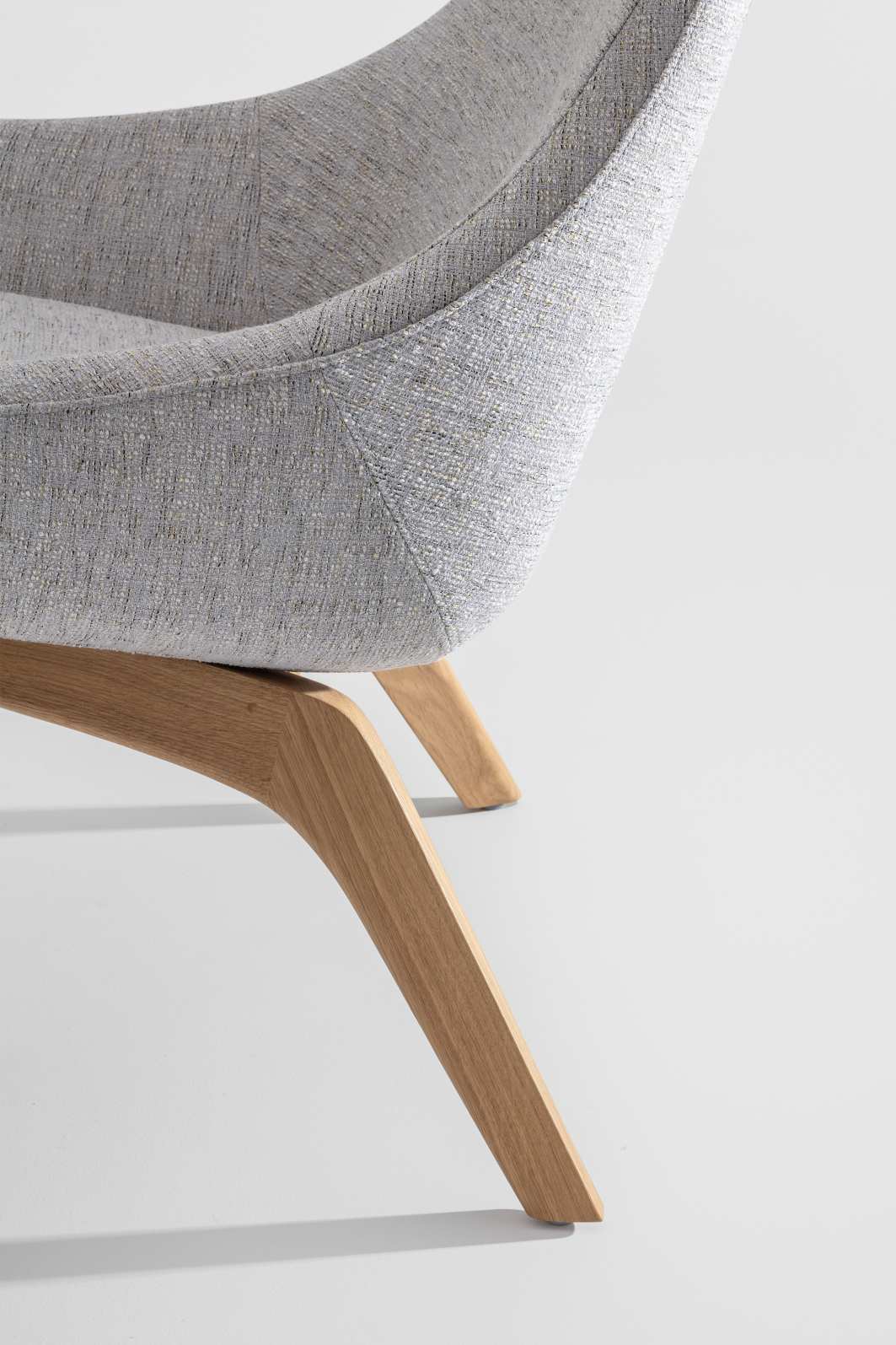 Detailaufnahme des Morph Lounge Chair Sessels mit grauem Stoffbezug und hellen Holzbeinen.
