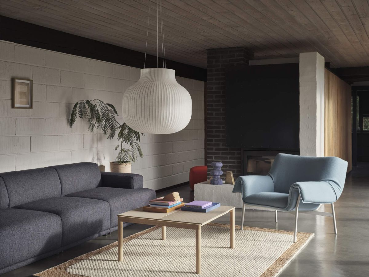 Wohnzimmer mit grauer Couch, blauem Sessel, Holztisch, Teppich und großer, weißer Pendelleuchte. Moderne Innenarchitektur.