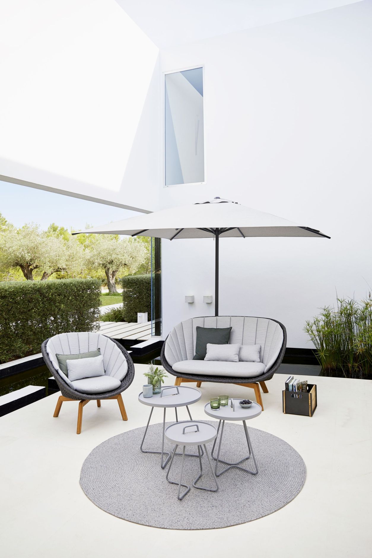 Graue Gartenmöbel-Lounge mit Sofa, Sessel, Beistelltischen, Sonnenschirm und Teppich für stilvolle Outdoor-Entspannung.