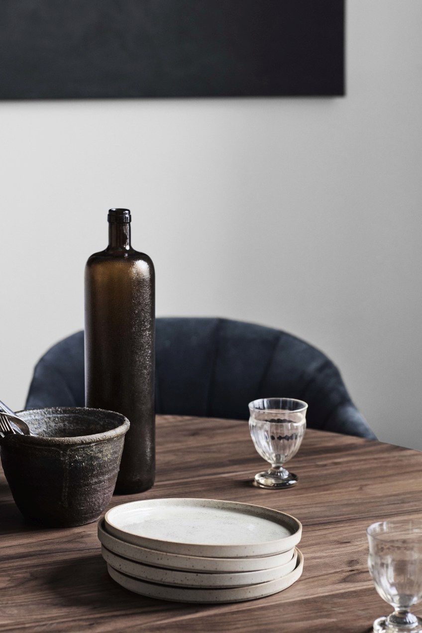 Detailaufnahme eines AndTradition Loafer Sessels SC24, teilweise sichtbar hinter einem gedeckten Holztisch mit Geschirr und Glas.