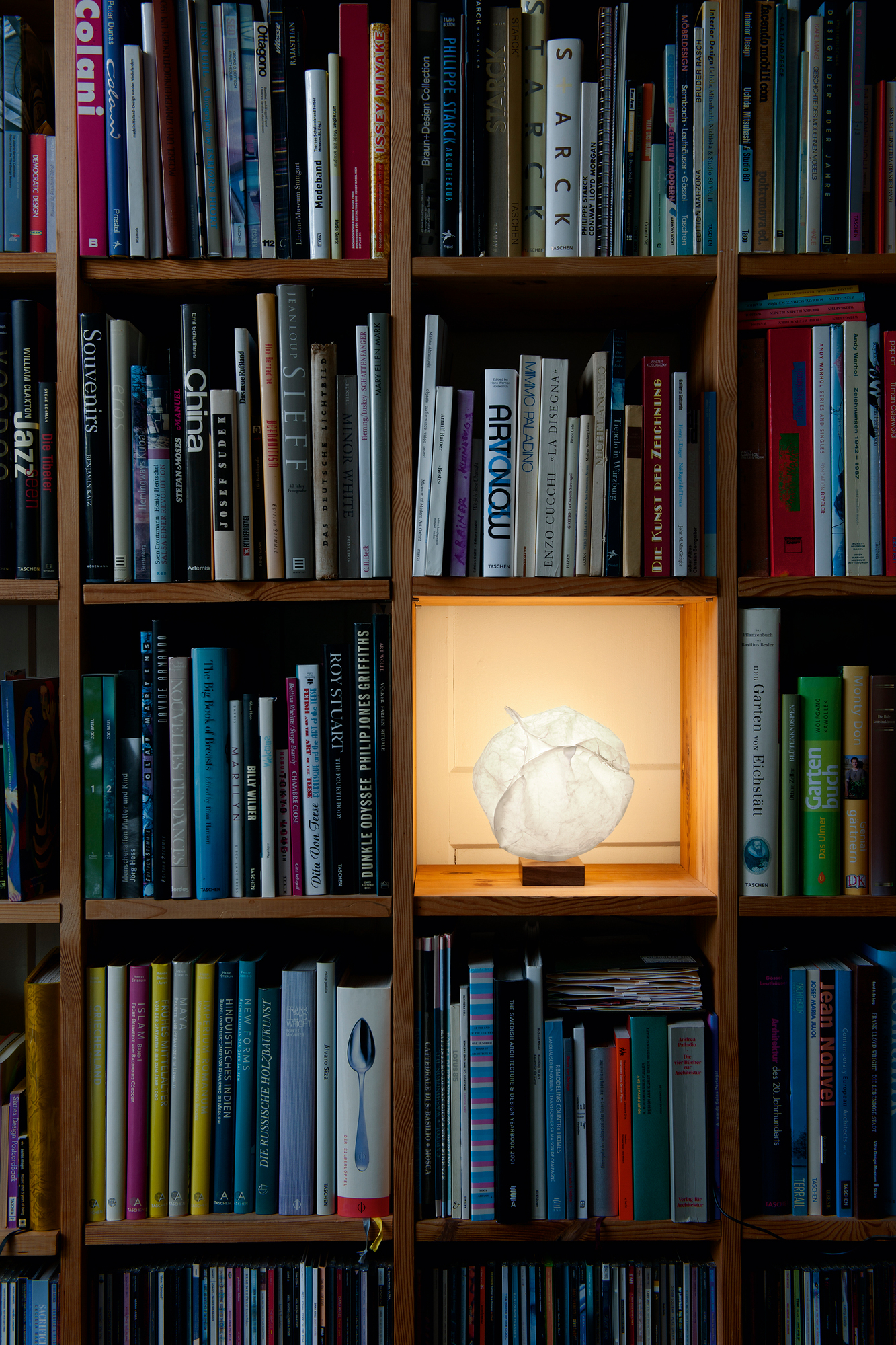 Dekorative Papierleuchte im Bücherregal, umgeben von Kunst- und Designbüchern, stimmungsvolle Beleuchtung für gemütliches Wohnambiente.