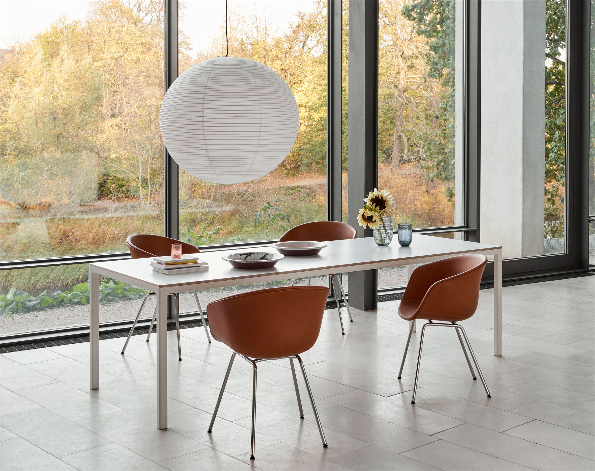Esszimmer mit HAY About A Chair AAC27 Stühlen in Braun, weißem Tisch und großer Fensterfront.