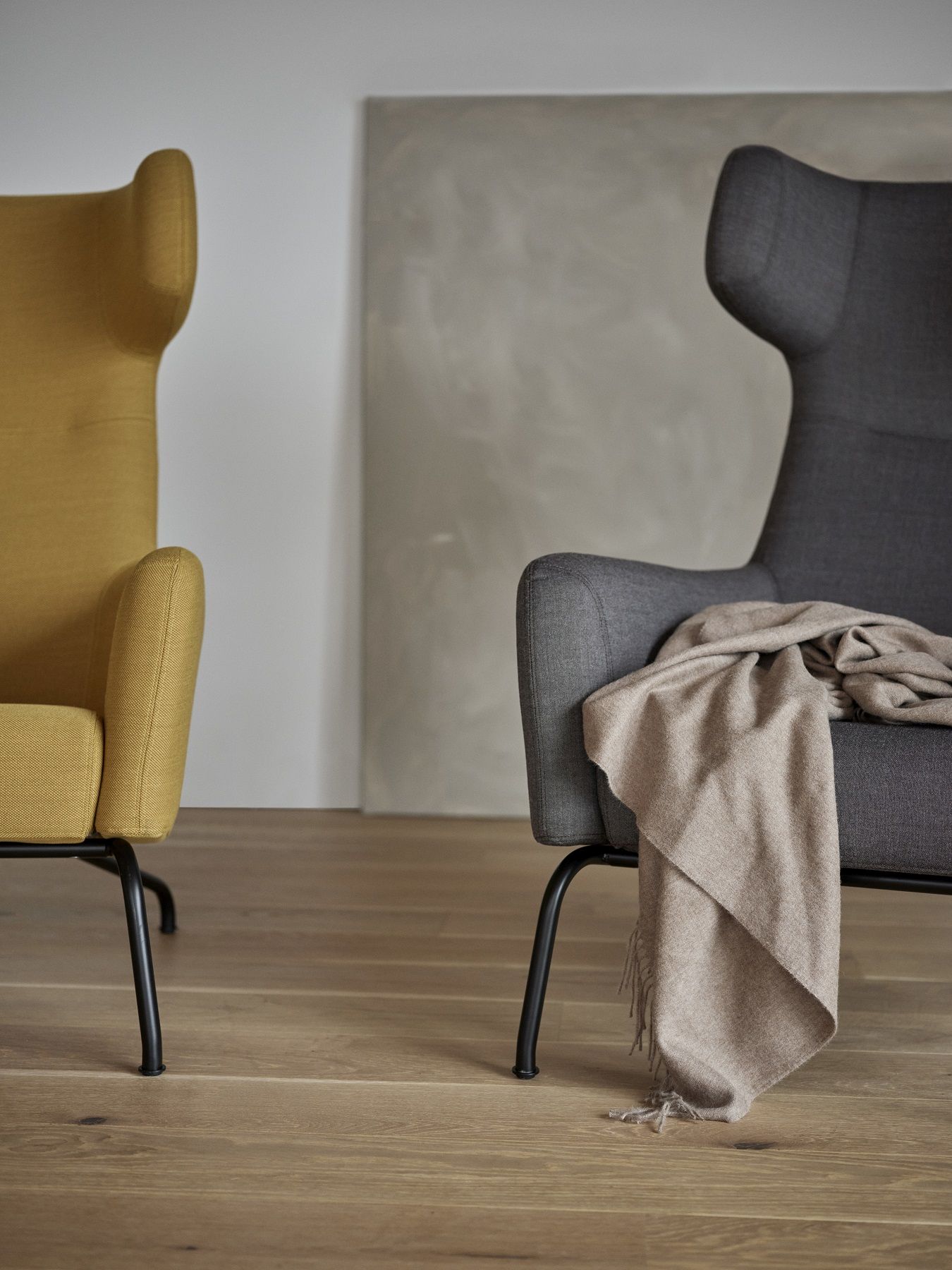 Zwei Ohrensessel: Gelber Havana Armchair und grauer Sessel mit Decke auf modernem Holzboden.
