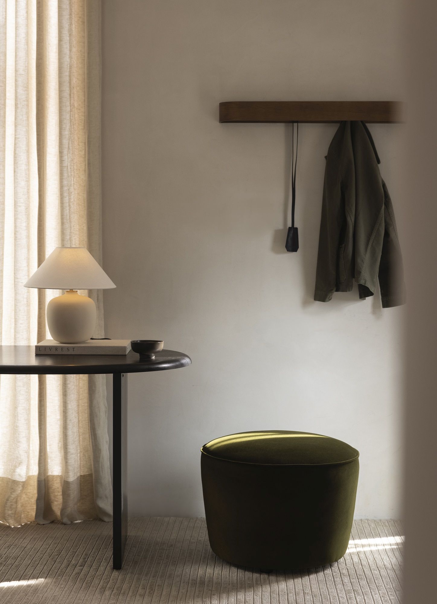 Nahaufnahme des Audo Copenhagen Eclipse Desk Schreibtischs mit Lampe, Buch und grünem Hocker in minimalistischem Interieur.