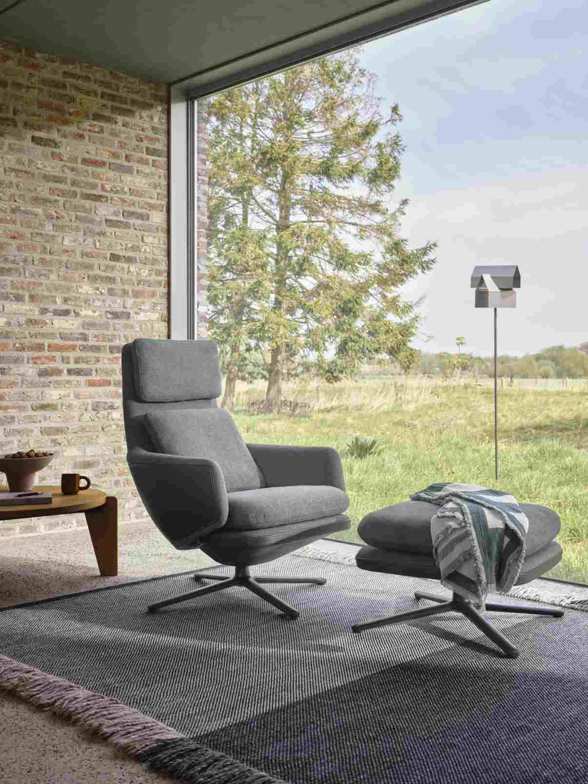 Grand Repos Sessel mit Ottoman in Rauchblau, Premium Leder und Kontrastnaht vor Fenster.