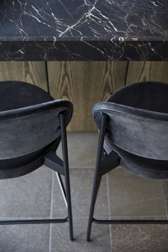 Detailaufnahme von zwei schwarzen Series 430 Barhockern mit Fußstütze vor einer Küchentheke mit Marmorplatte.