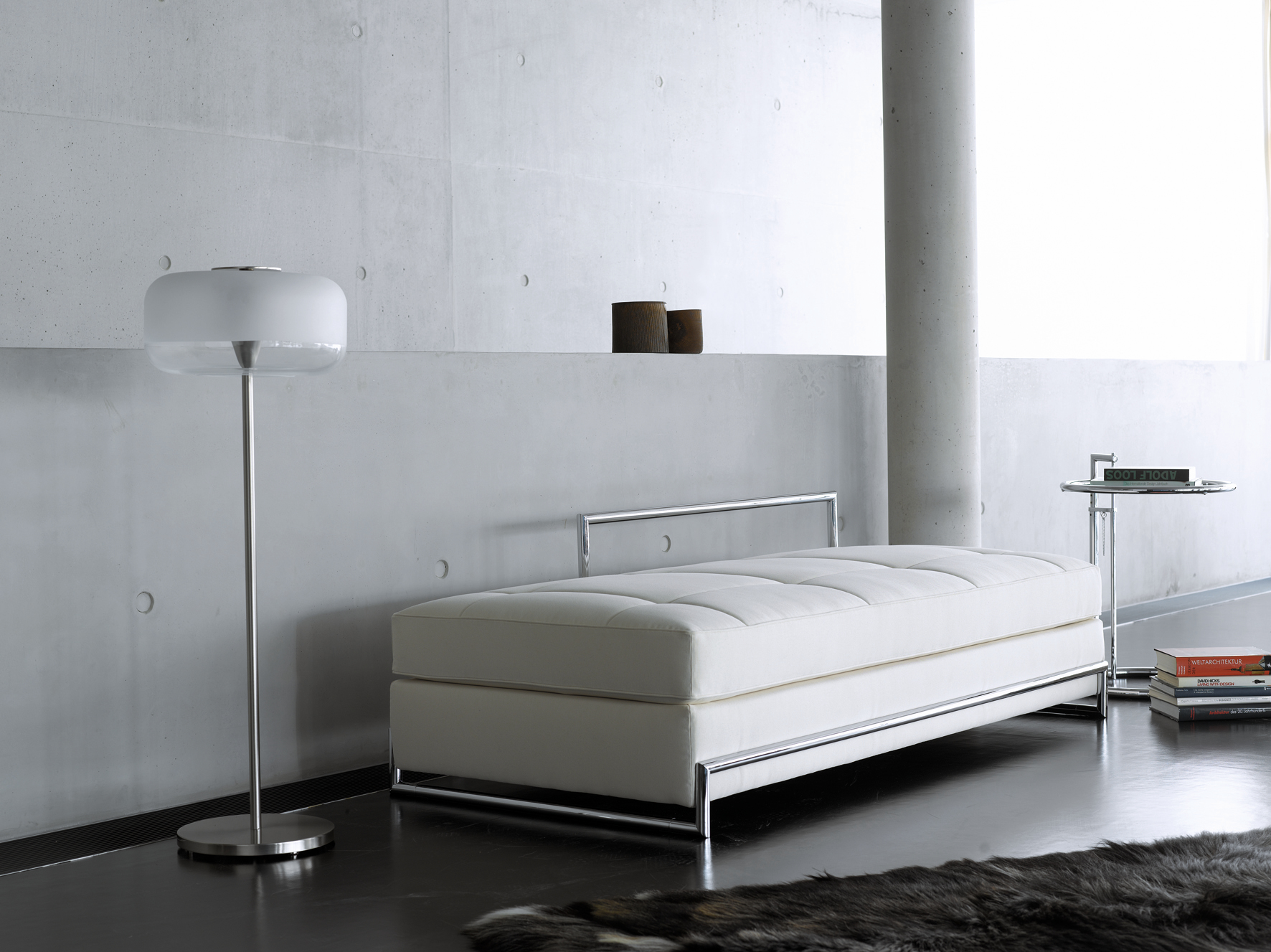 Adjustable Table E1027 Beistelltisch von ClassiCon neben weißer Ottomane und Stehlampe im modernen Interieur.