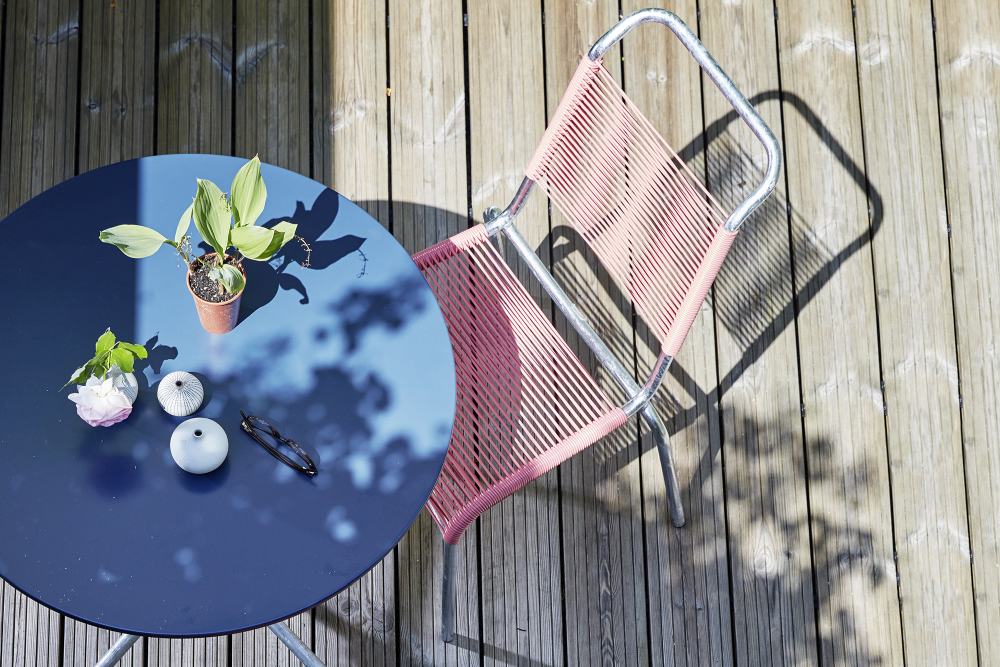 Altorfer Stuhl Outdoor in Verkehrsrot (RAL 3020) neben blauem Gartentisch auf Holzterrasse, Top-Ansicht.