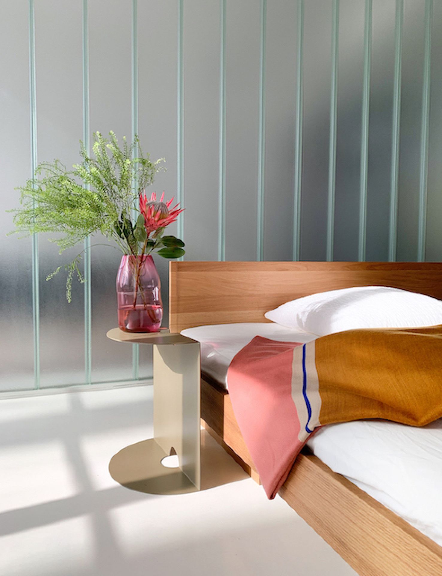 Helles Schlafzimmer mit Holzbett, farbiger Tagesdecke und Vase mit Blumen auf modernem Beistelltisch.