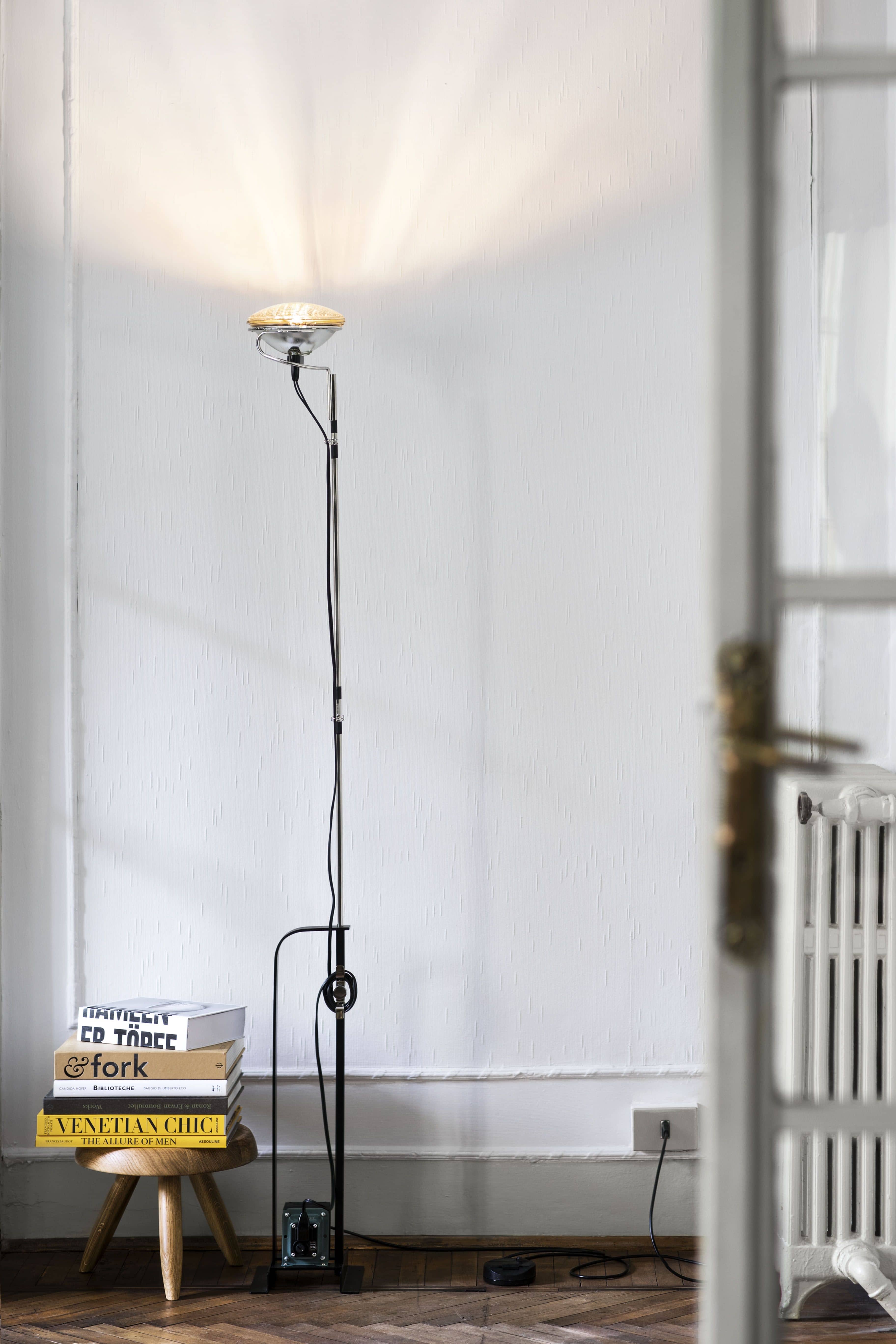 Stehlampe im Interieur: Moderne Stehleuchte mit rundem Lampenschirm, Bücherstapel und Holzhocker im Wohnzimmer.