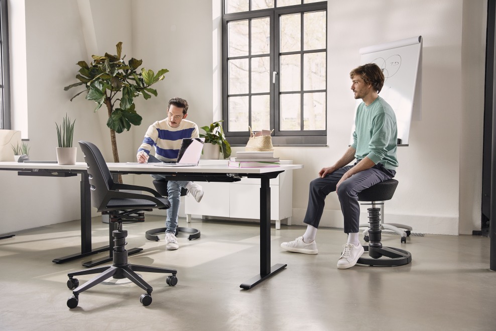 Numo Task Bürodrehstuhl von Aeris im modernen Büro, ergonomischer Arbeitsplatz mit höhenverstellbarem Schreibtisch und Stehhocker.